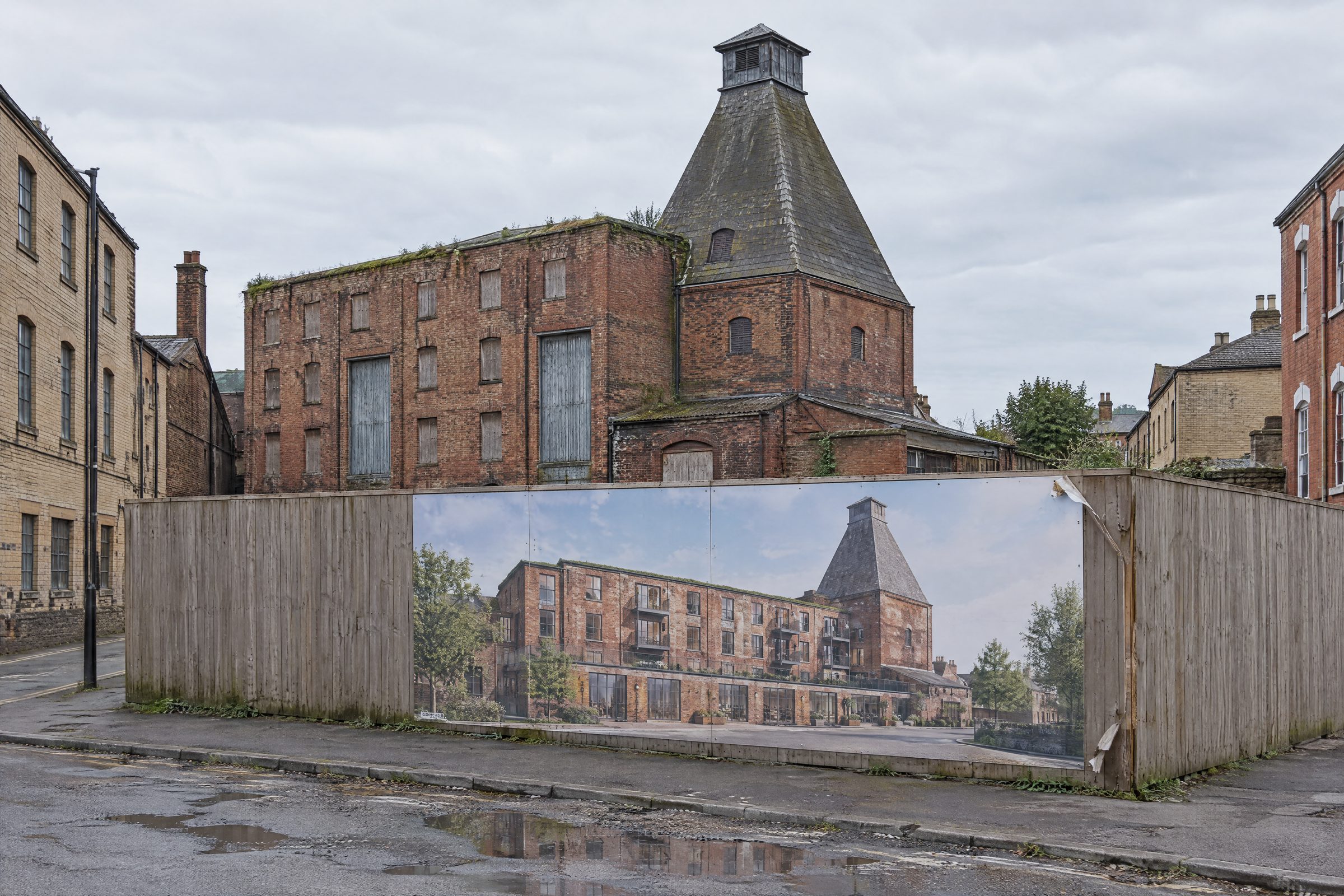 The Old Maltings, a disused Victorian maltings with its pyramid kiln, behind hoarding showing the proposed scheme