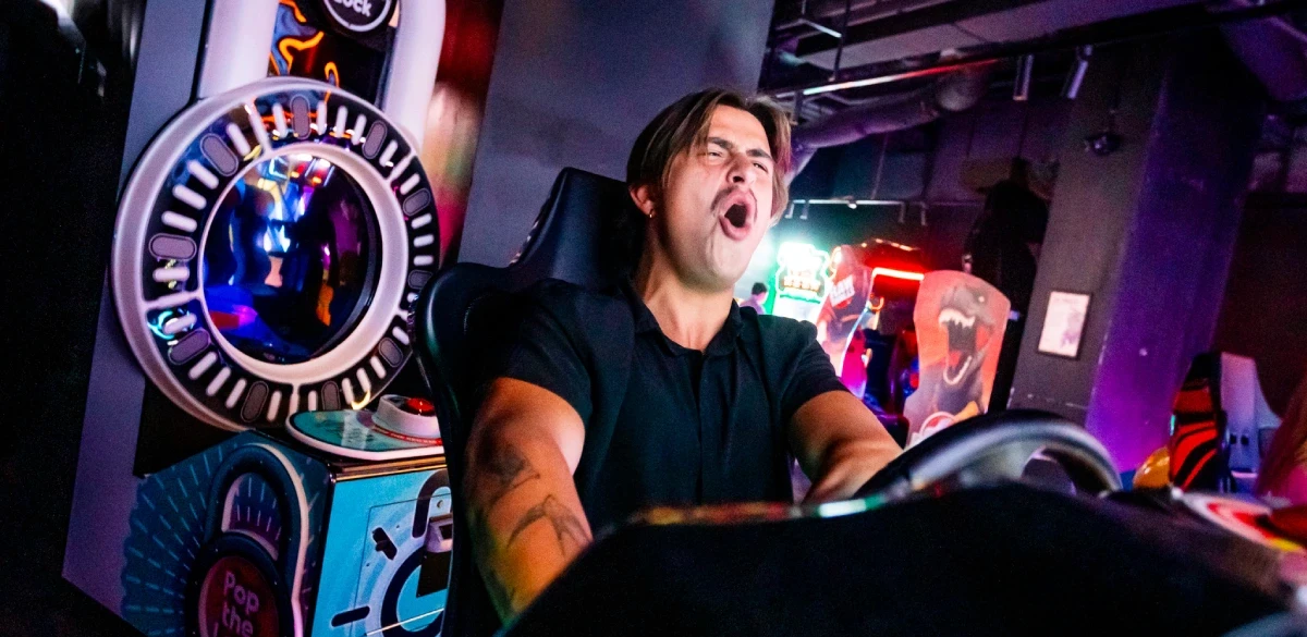 A man grinning as he plays a racing arcade cabinet
