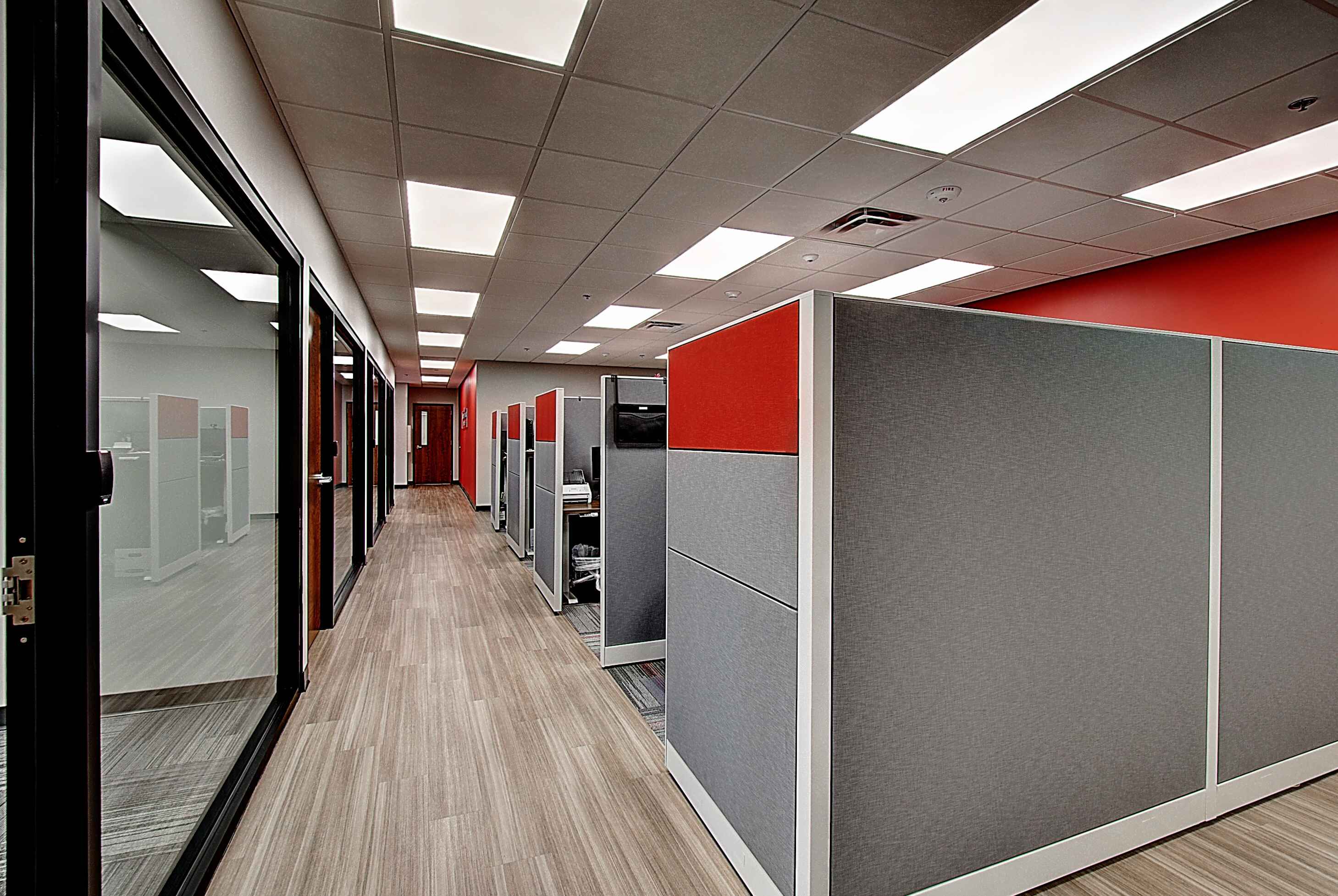 Brightly lit office hallway with red and gray partitioned spaces and glass doors. Modern design and decor.
