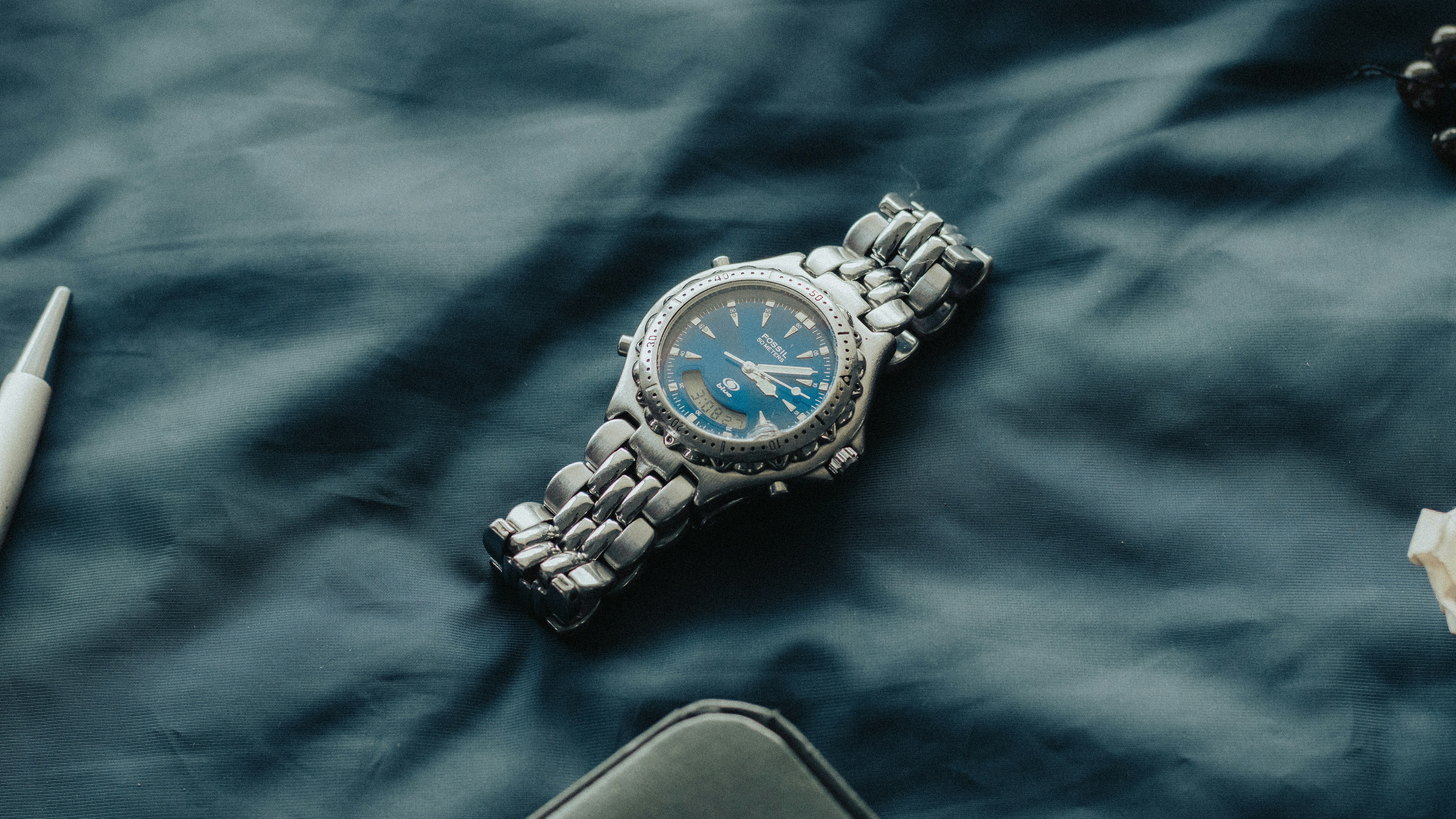 a watch sitting on top of a bed next to a pen