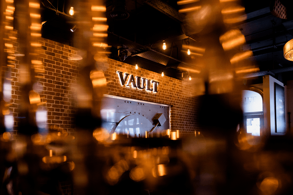 The illuminated Vault Shenfield sign above the DJ booth, glowing against the vibrant club atmosphere.