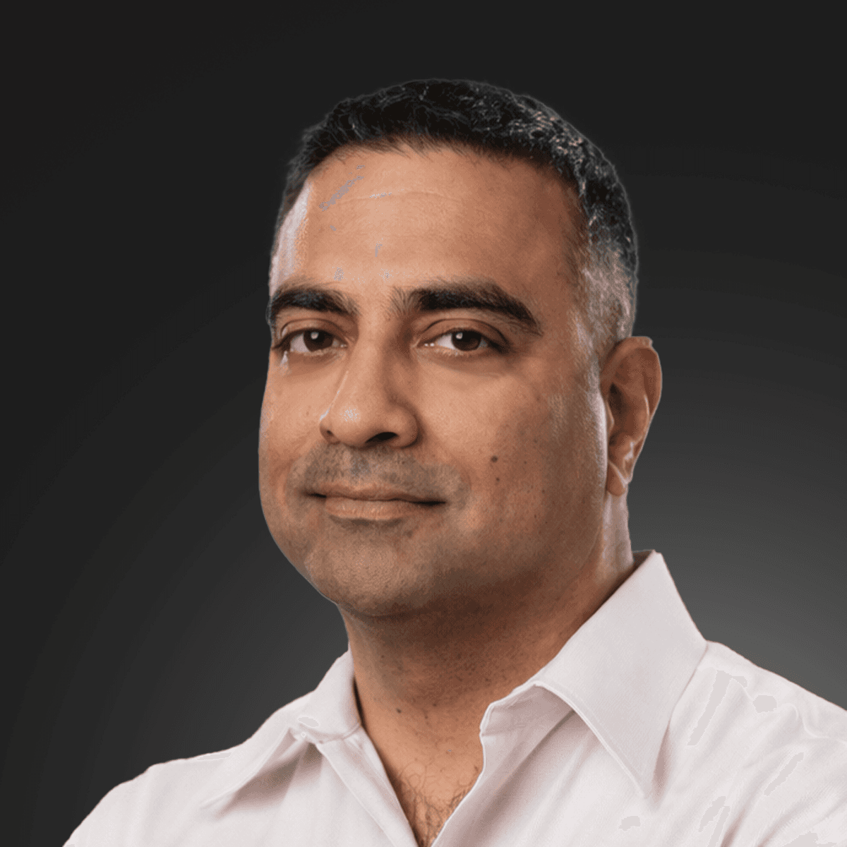 Smiling young man with curly hair, wearing a dark hoodie, against a softly lit background.