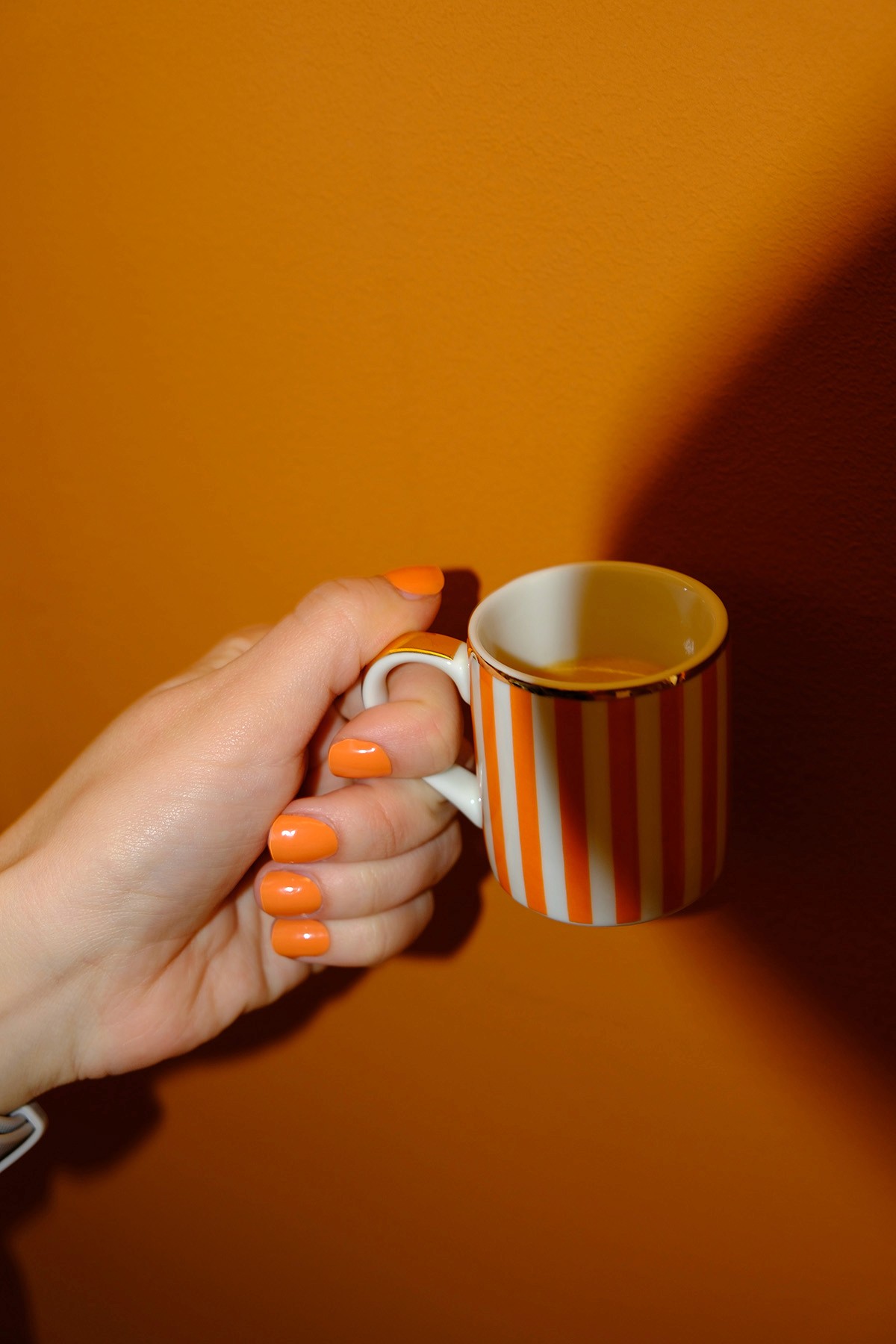 Artsy Espresso-Häferl und orange Fingernägel vor oranger Wand