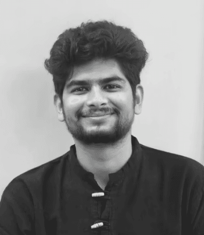Smiling young woman with long hair standing against a dark green background, holding a finger to her chin.