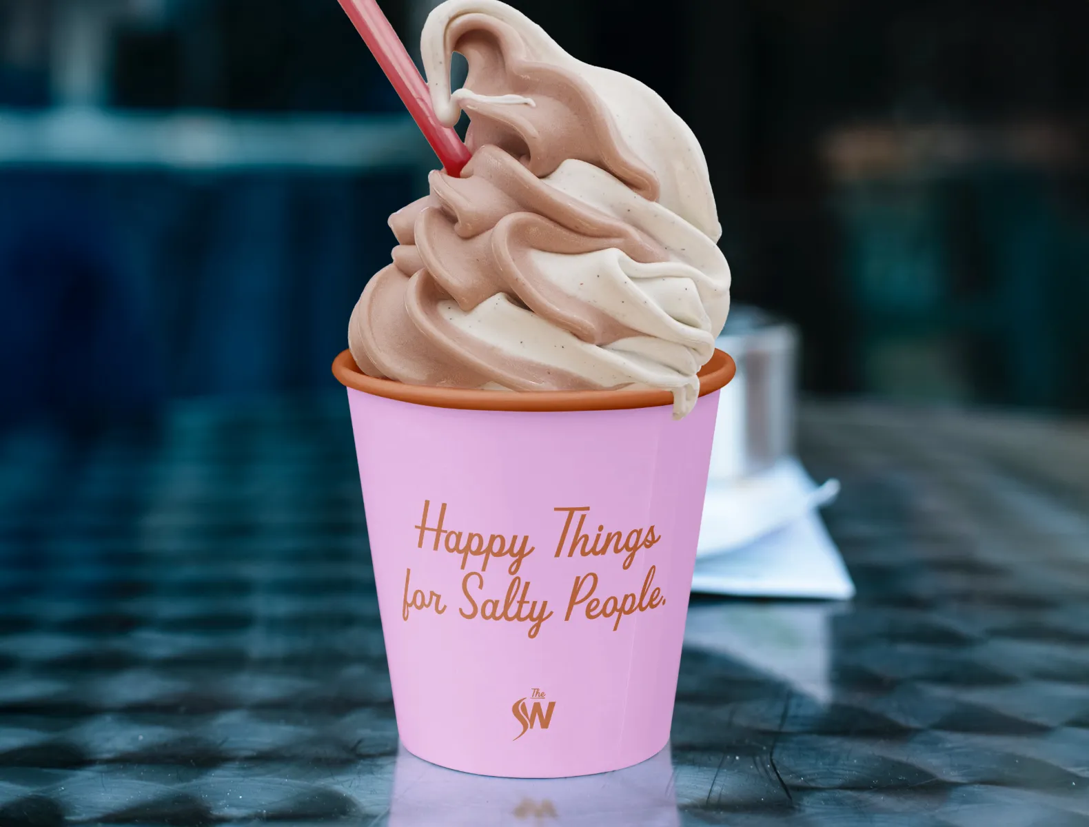 A pink icecream cup with chocolate swirl soft serve in it. The cup says "Happy Things for Salty People" with the SW monogram.