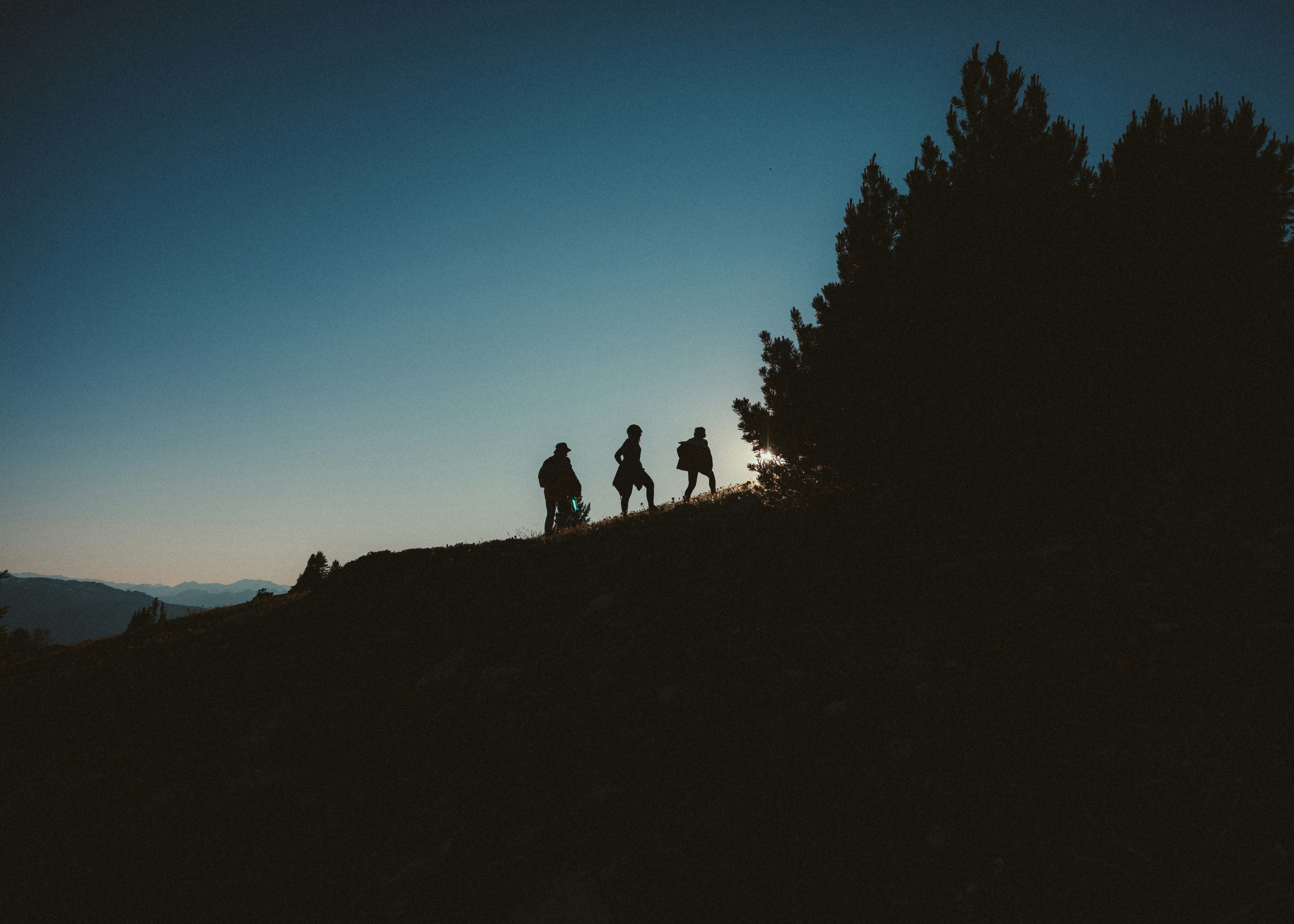 Hikers silhouetted against a clear blue sky at sunset.