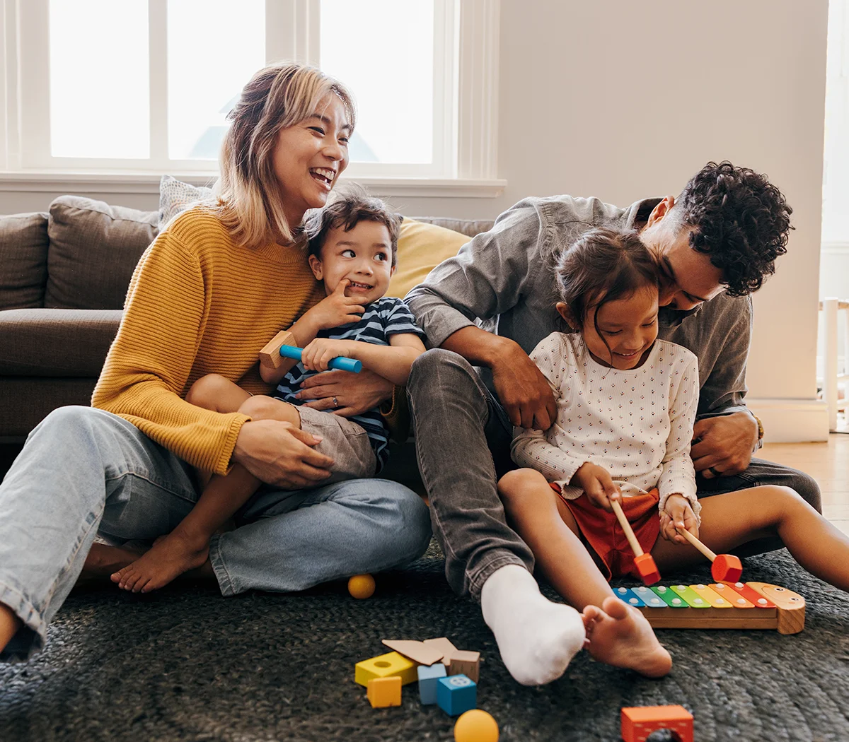 A happy family with a mum and dad and 2 kids, playing in the living room.