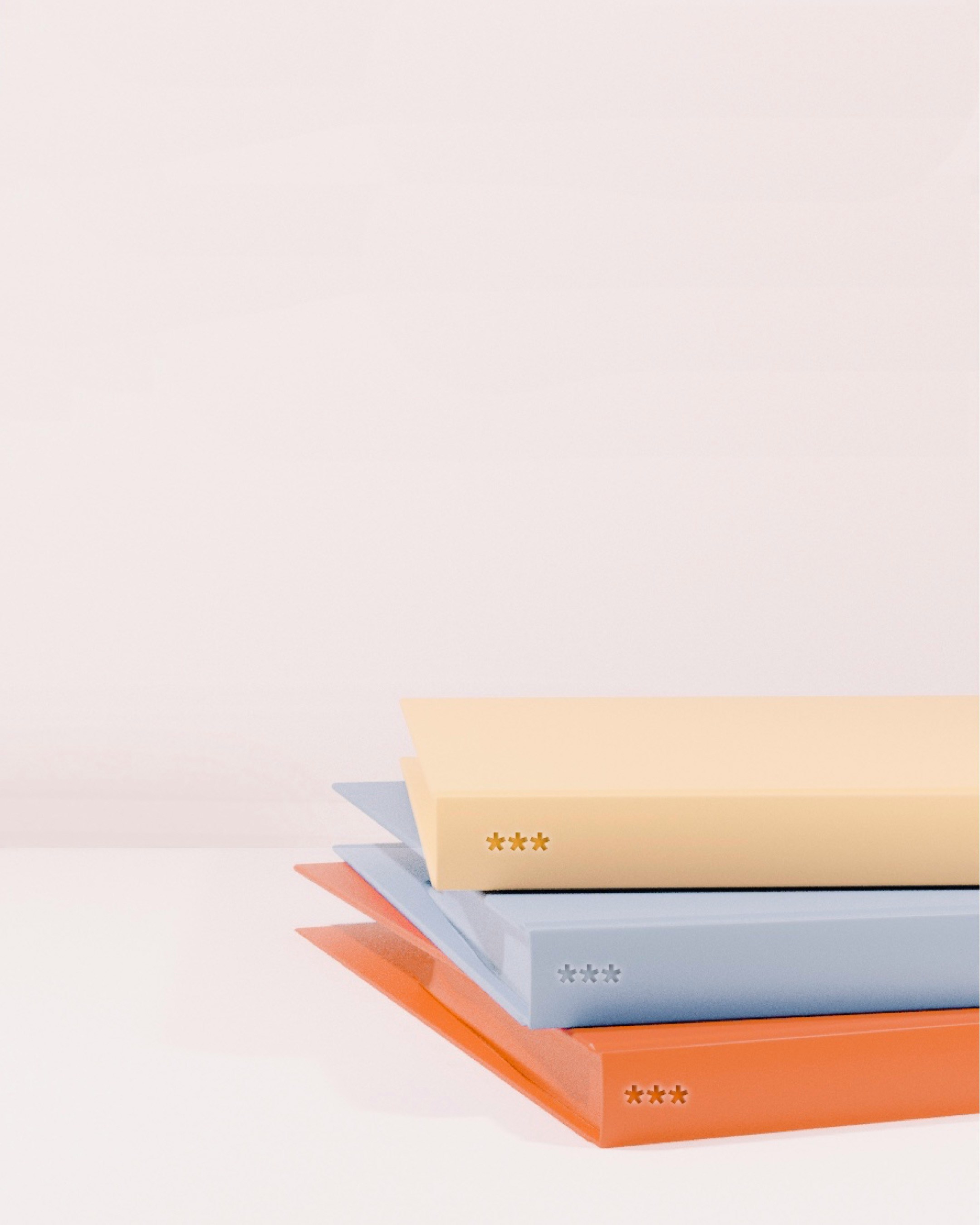 tack of three colorful notebooks in yellow, blue, and orange on a white surface