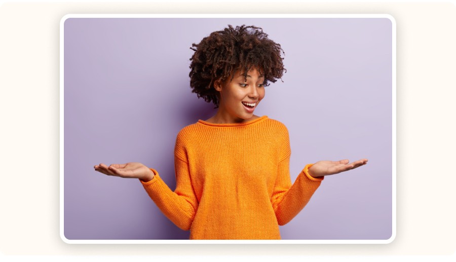 Smiling woman in orange sweater shrugging with both hands raised