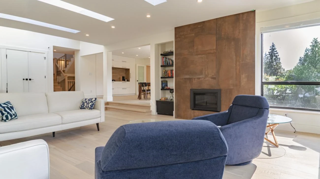 Open concept living area with fireplace, skylights, hardwood floors, and connection to dining space in Vancouver custom built home