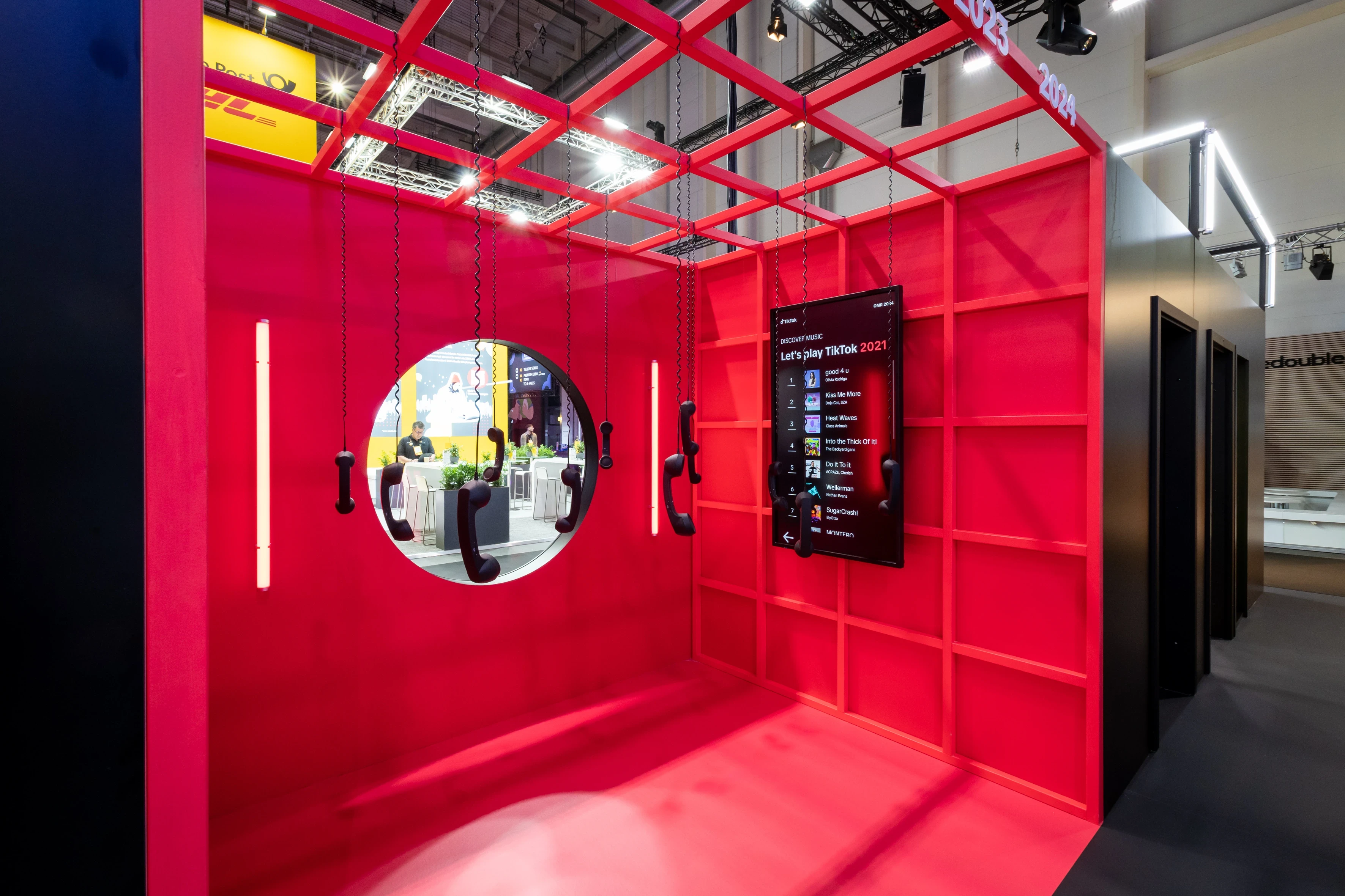 Red grid room with hanging telephone receivers, round window and playlist screen at the TikTok booth at OMR.