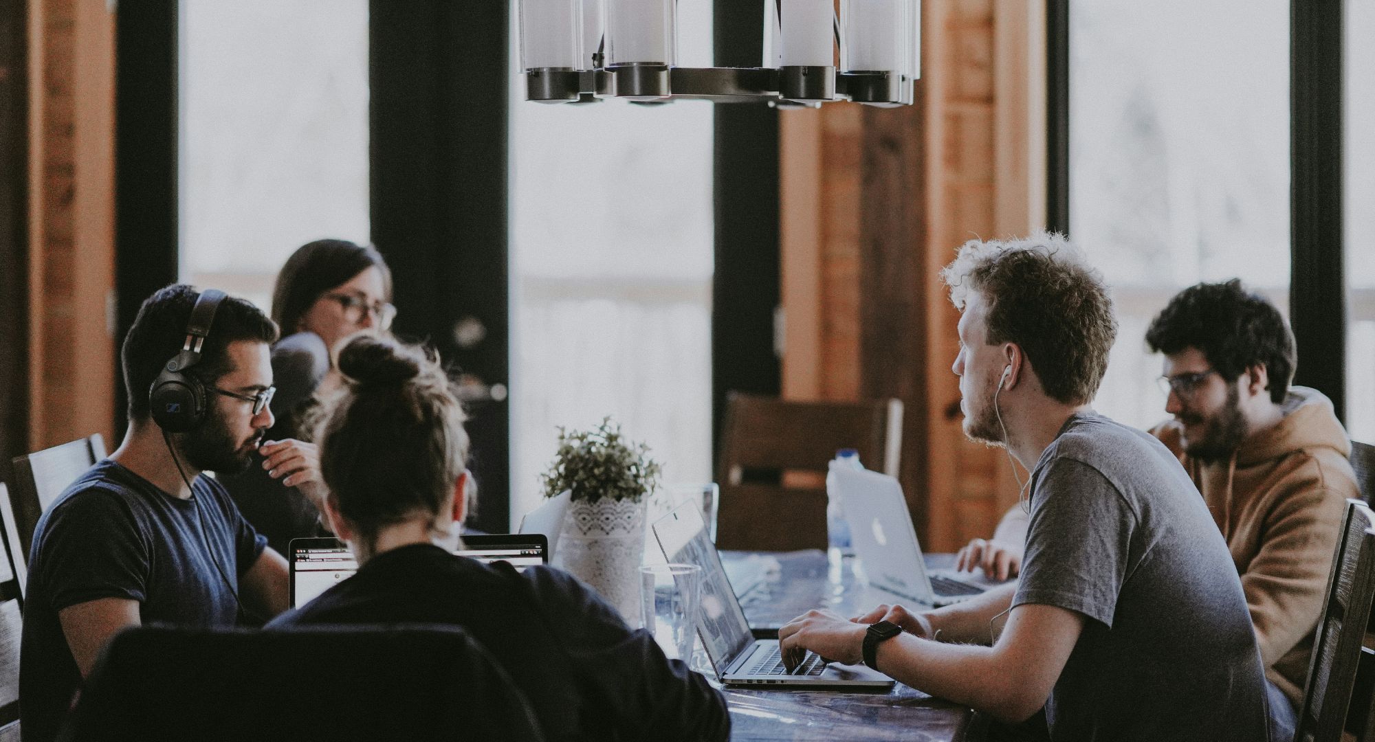 pessoas sentadas ao lado uma das outras trabalhando em uma mesa de sala