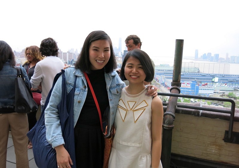 portrait of two woman on a balcony with people behind them