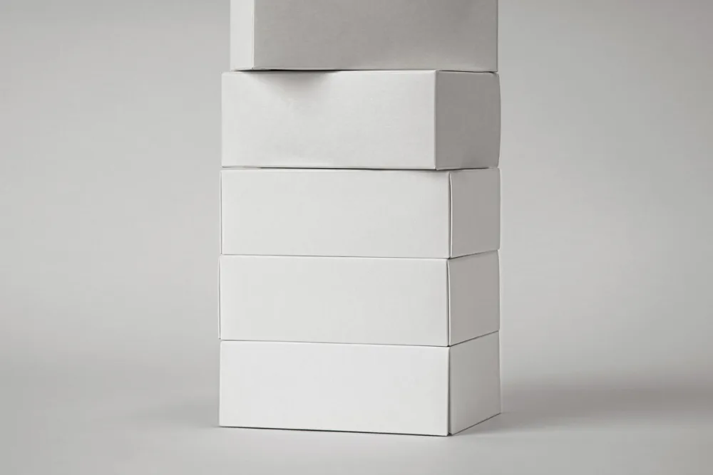Stack of kraft cardboard boxes with bold black typography, arranged vertically against a dark background. Minimal lighting highlights the texture and structure of the packaging.