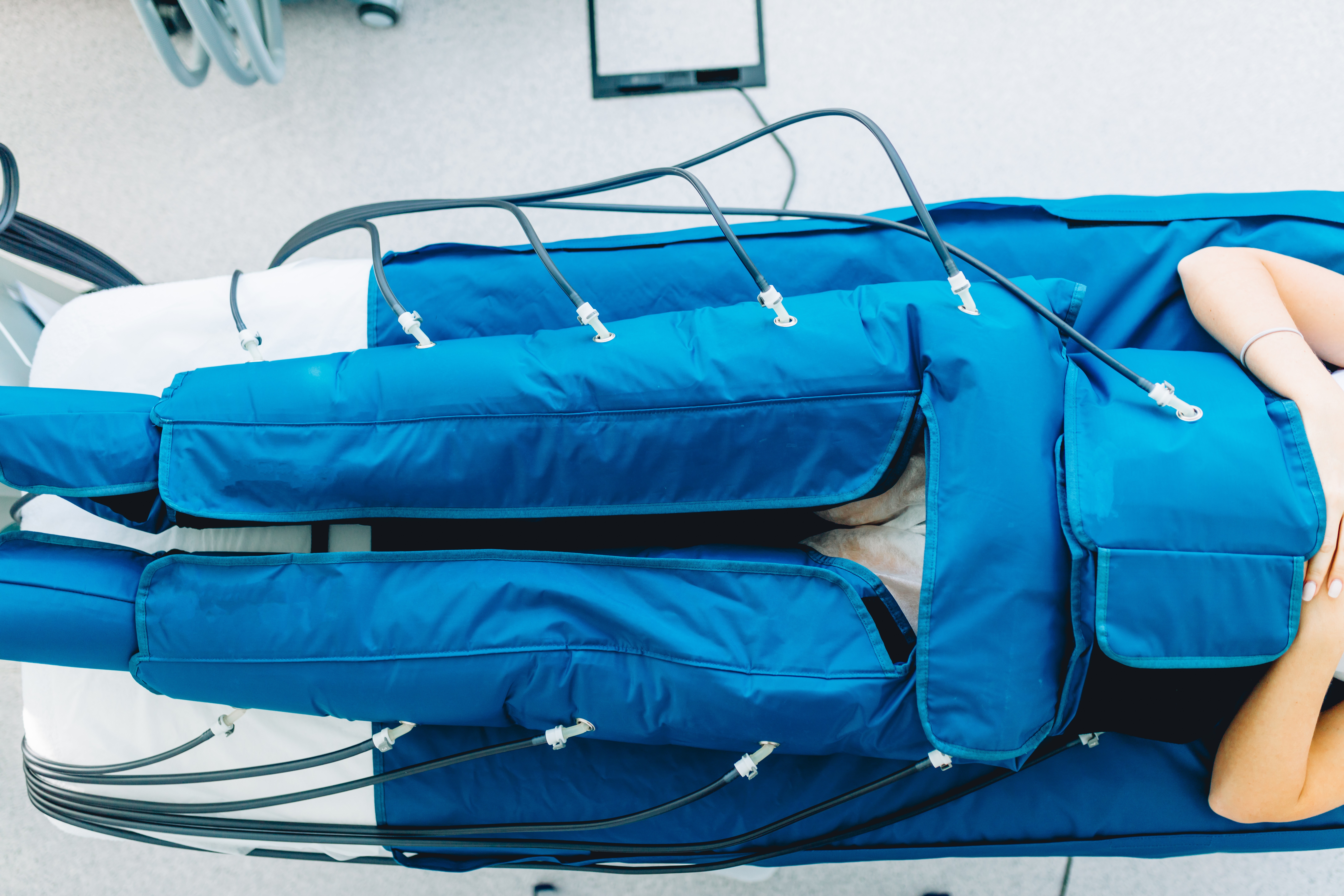 Tratamiento estético de presoterapia en Espacio Yutori, San Fernando. Una persona recostada boca arriba usa mangas de compresión azules para piernas y abdomen conectadas a un equipo profesional para mejorar la circulación y reducir edemas.