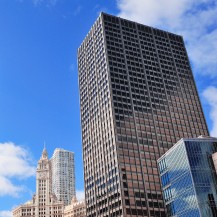 The image showcases several modern skyscrapers against a bright blue sky with scattered clouds, highlighting urban architecture in a city setting.