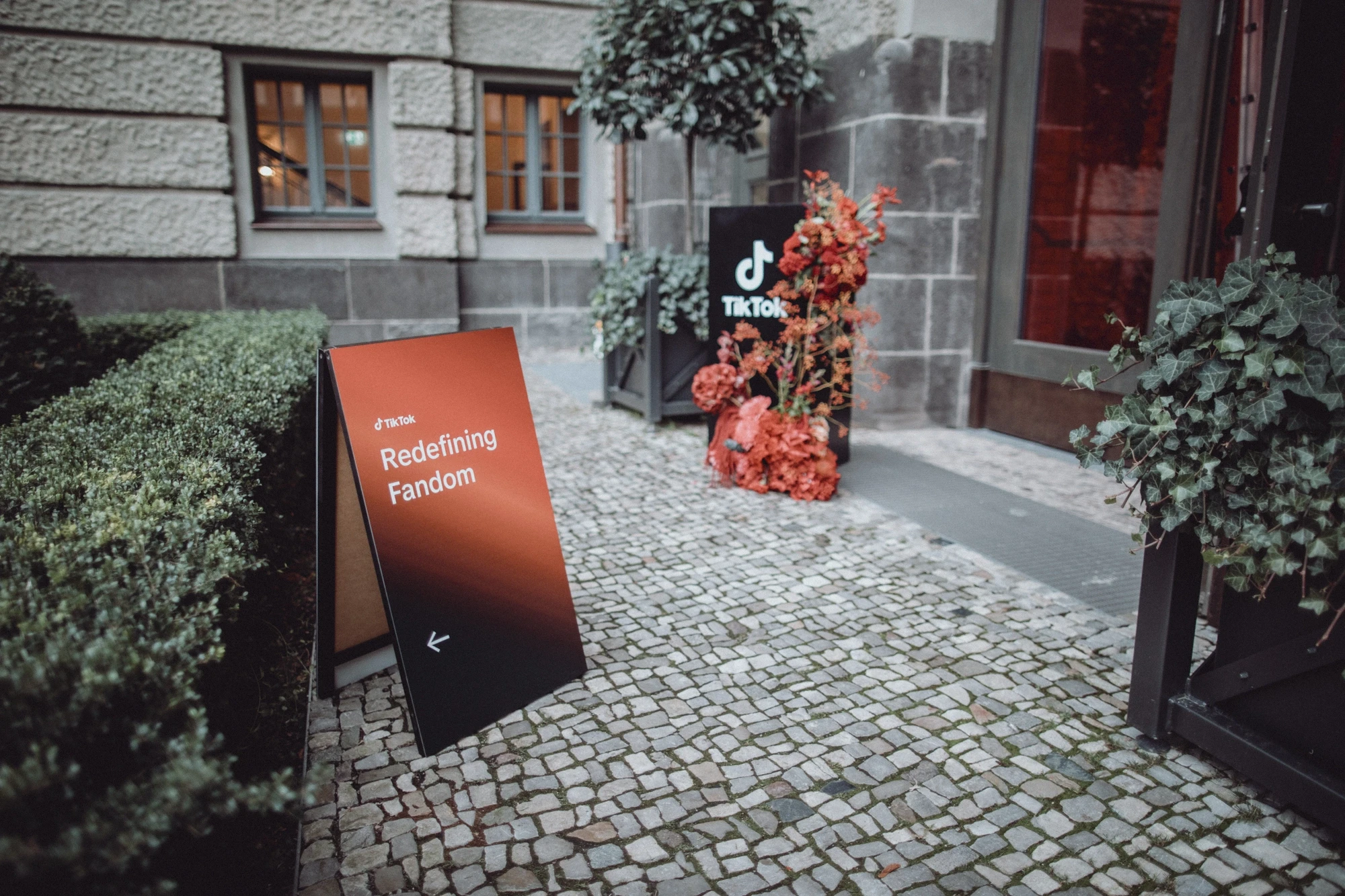 Redefining Fandom sign and TikTok pillar with red flowers at the cobblestone entrance.