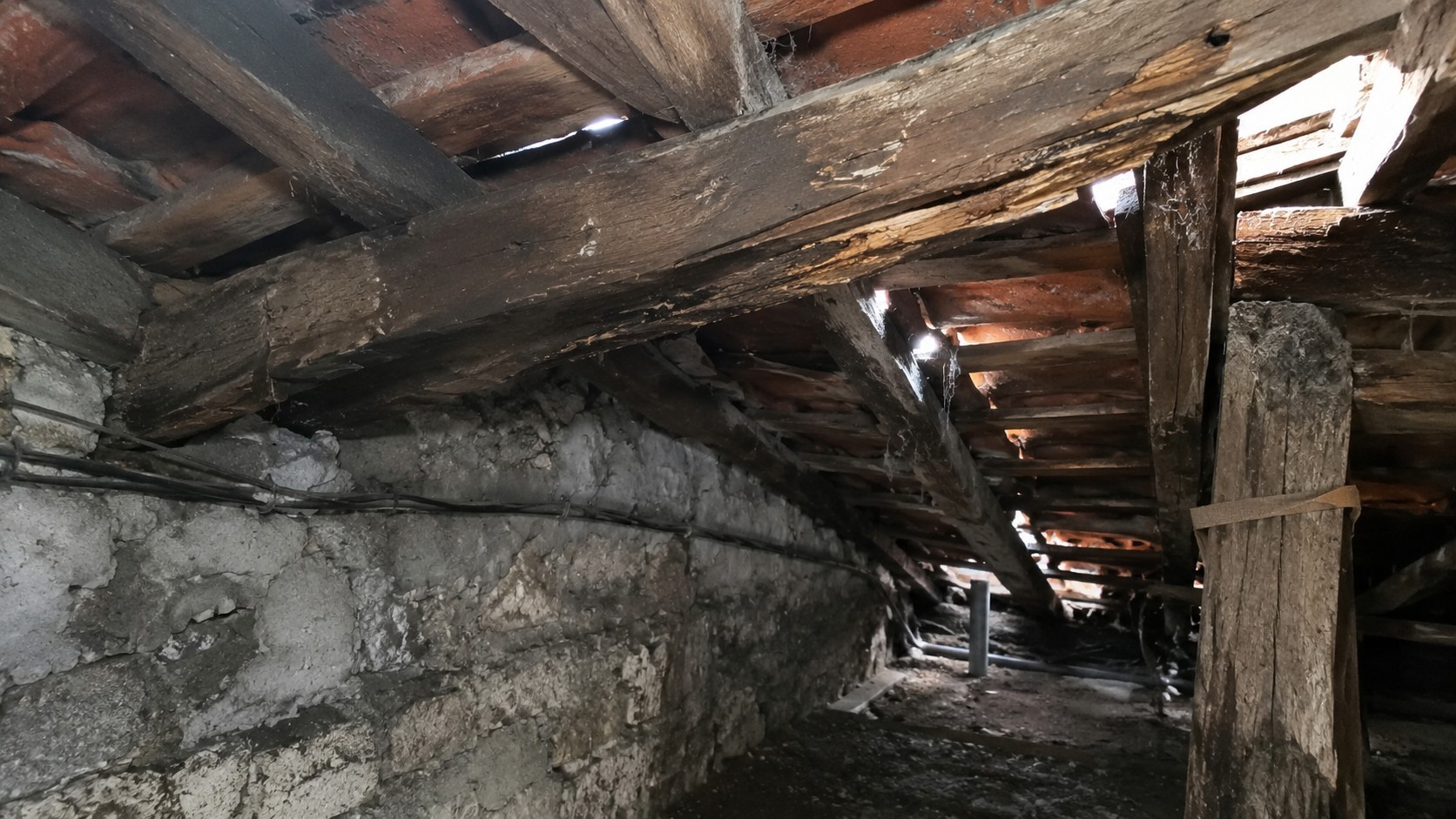 Charpente ancienne affaiblie sous toiture à Paris avec poutres en bois fissurées, traces d’humidité et signes d’alerte avant une fuite.