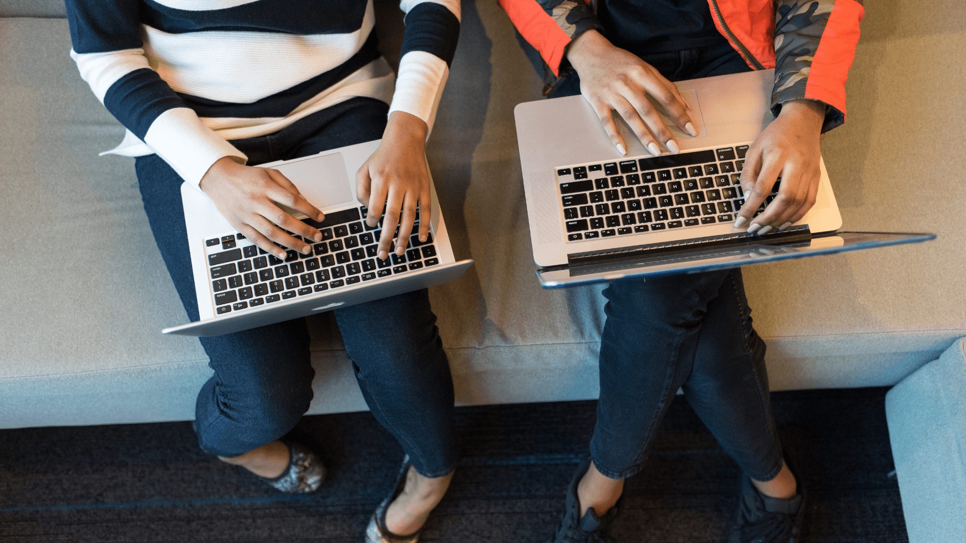 Two people sitting on a couch with laptops on their laps