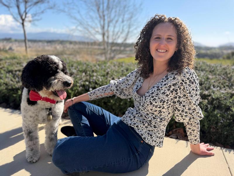 Image of Theresa smiling and sitting with a black and white dog