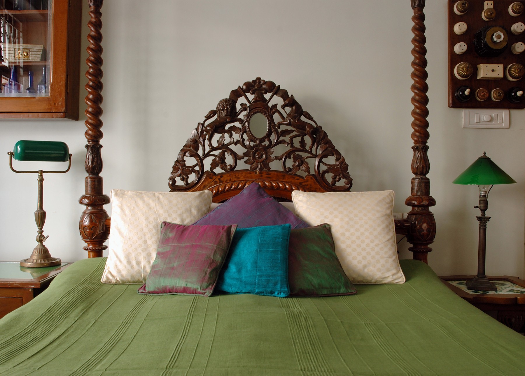 Carved teak four-poster bed with layered silk cushions and vintage bedside lamps in a heritage-style bedroom.