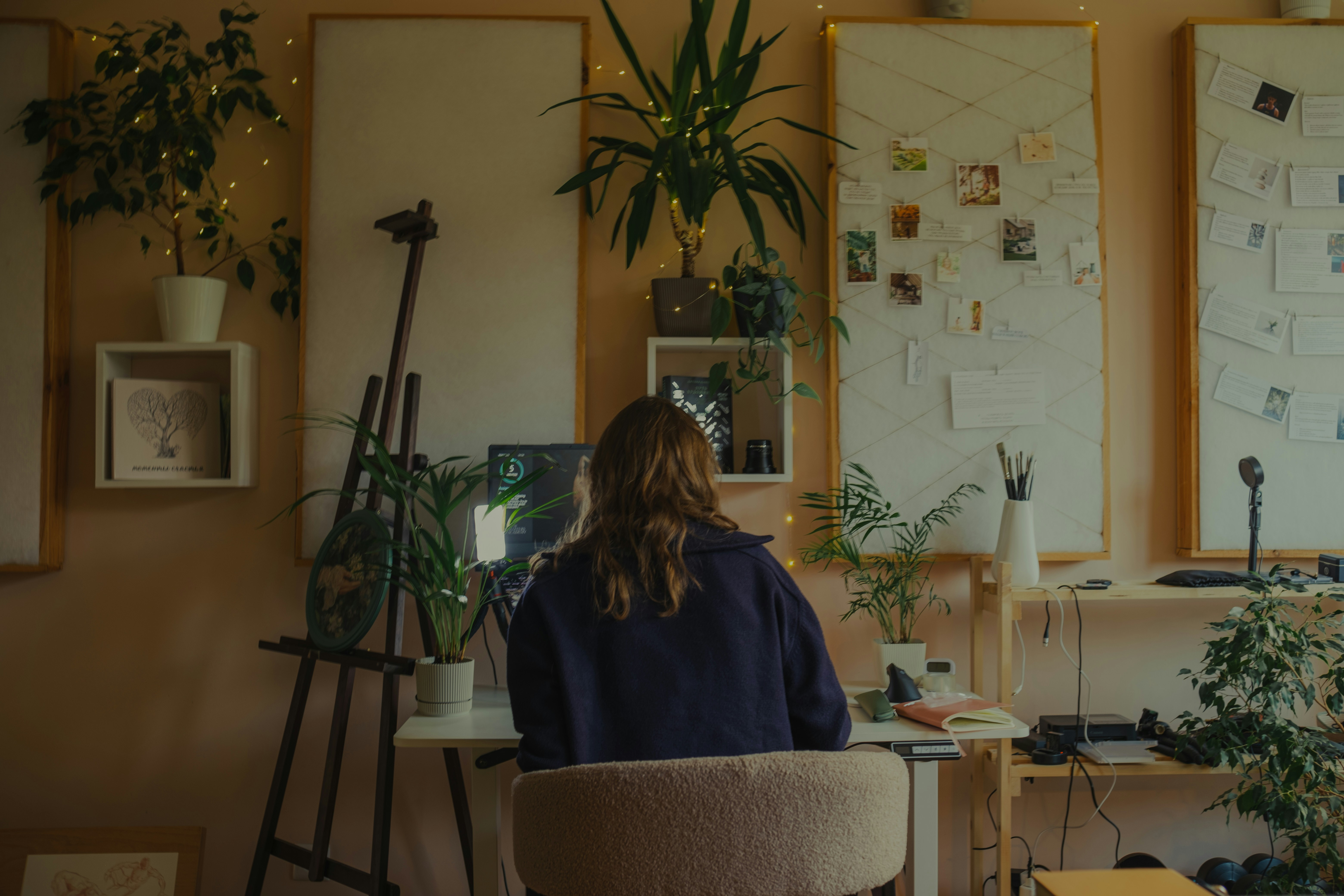Woman working at a desk in a plant-filled studio.