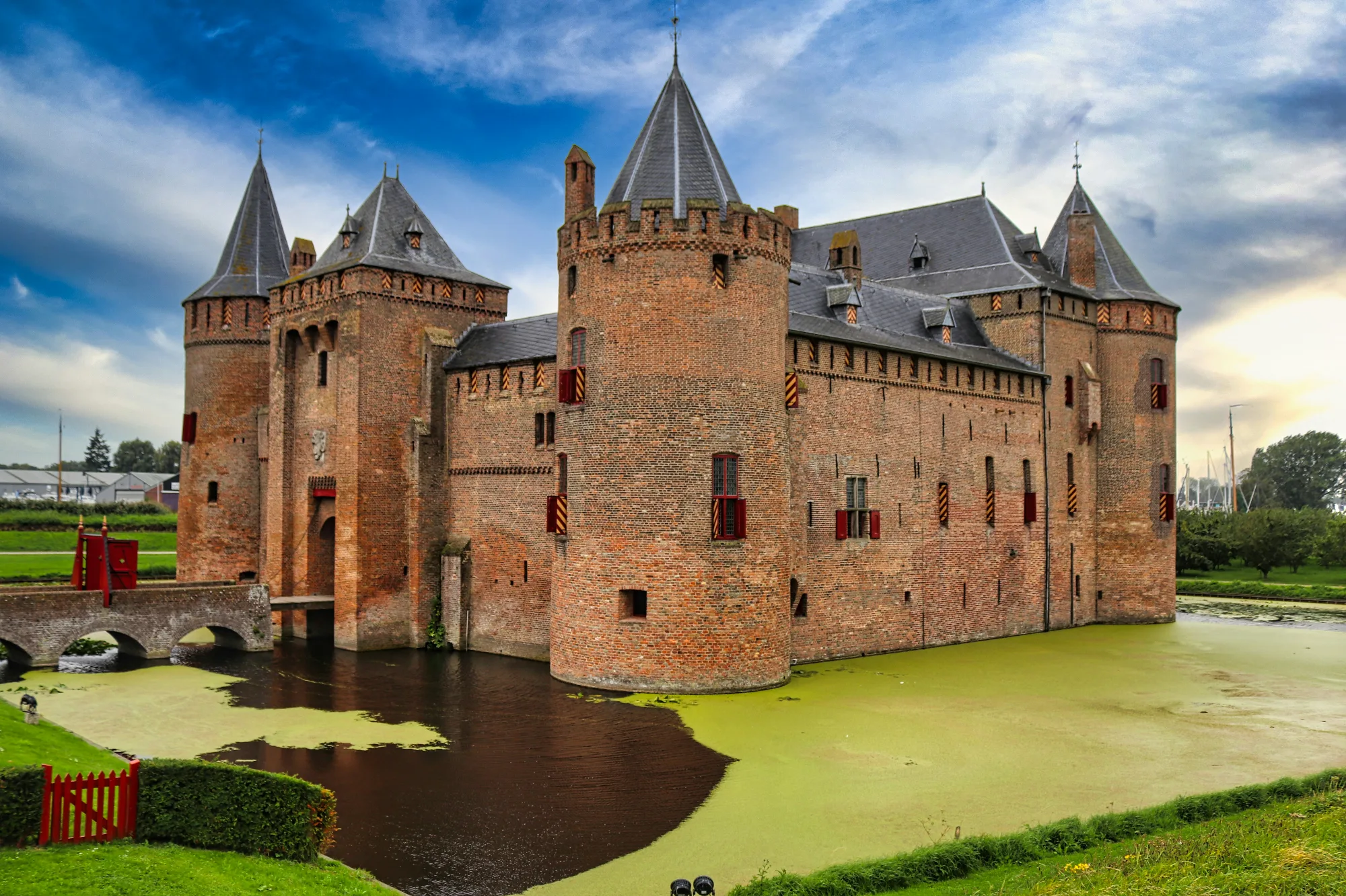 Medieval brick castle with towers surrounded by a moat, accessed by a bridge. Historic Dutch architecture.