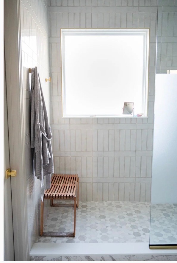 A serene outdoor seating area with two chairs, surrounded by lush greenery and a glassed-in structure.