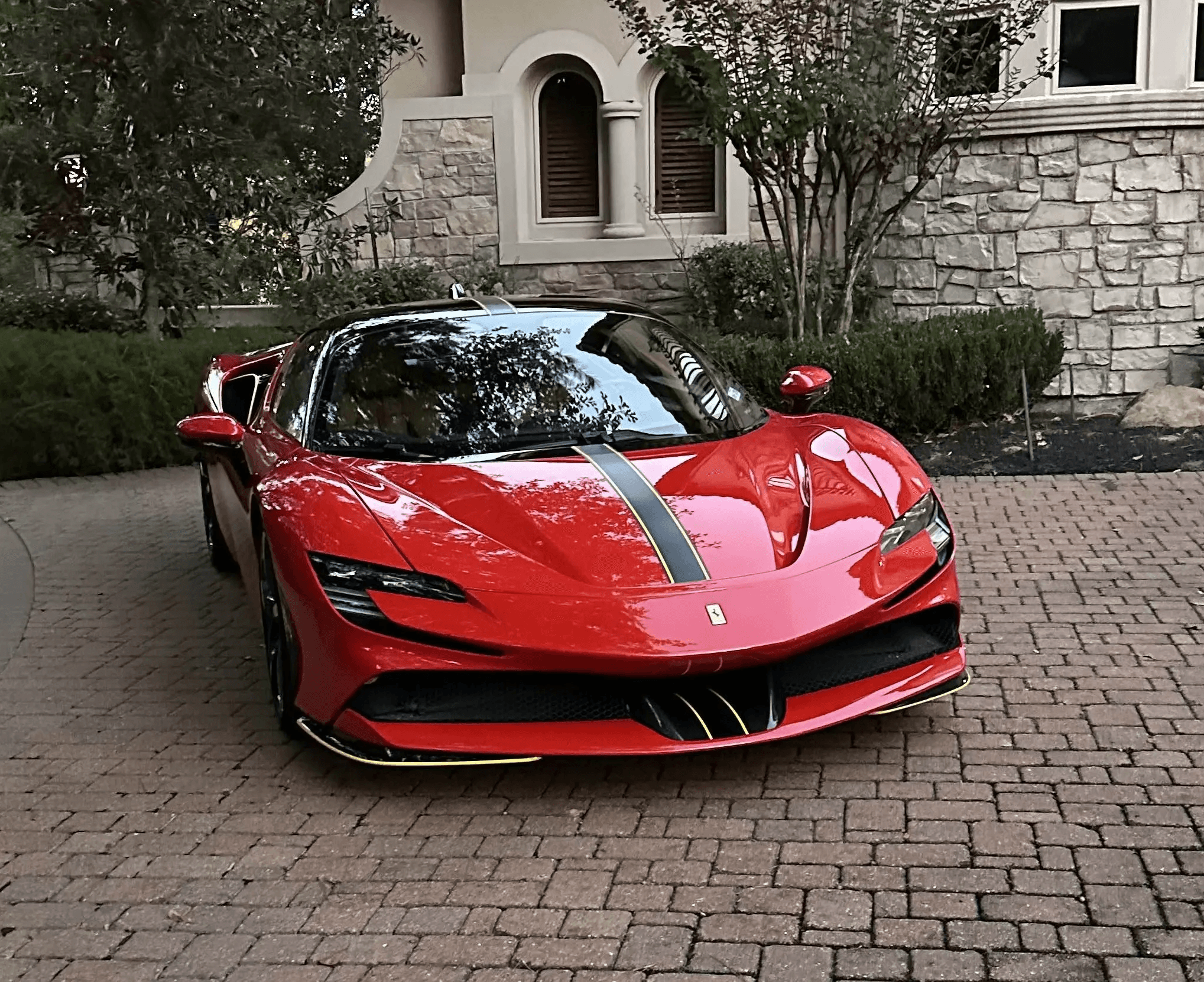 A red Ferrari SF90 Stradale with a black center stripe parked on a brick driveway in Houston after receiving a high-end exterior detail.
