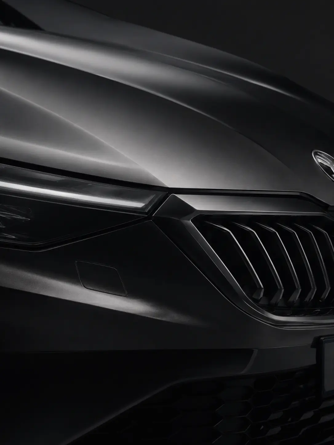 Detailaufnahme der Front eines dunklen Fahrzeugs mit schmalem LED-Scheinwerfer und großem vertikalen Kühlergrill von Skoda..