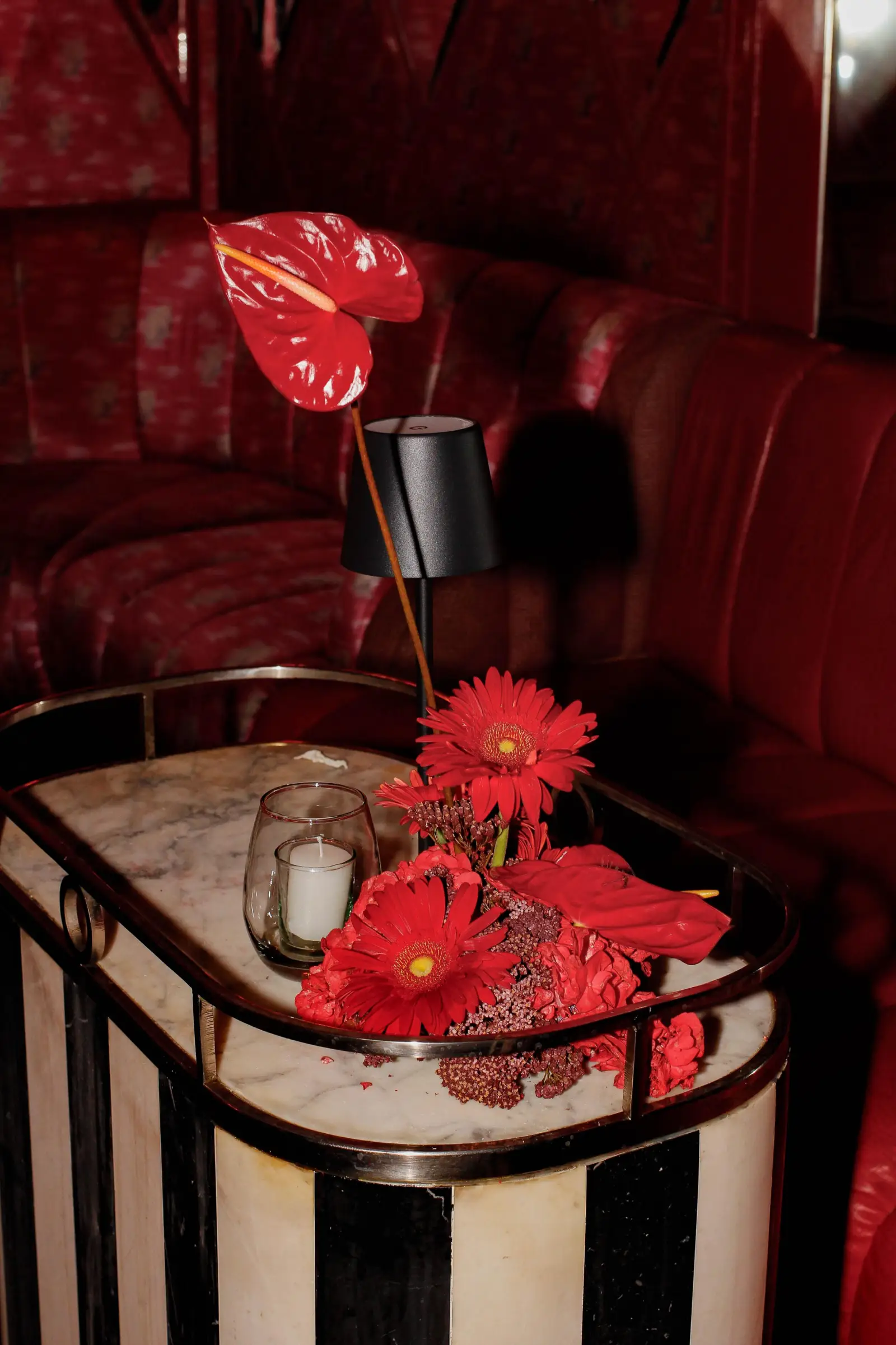 Centro de mesa con anturios y gerberas carmín sobre mueble de mármol.