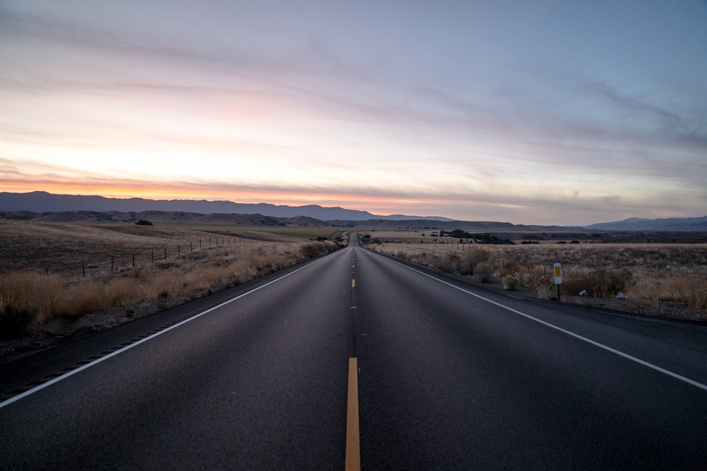 A two-lane road surrounded by plains just after sunset