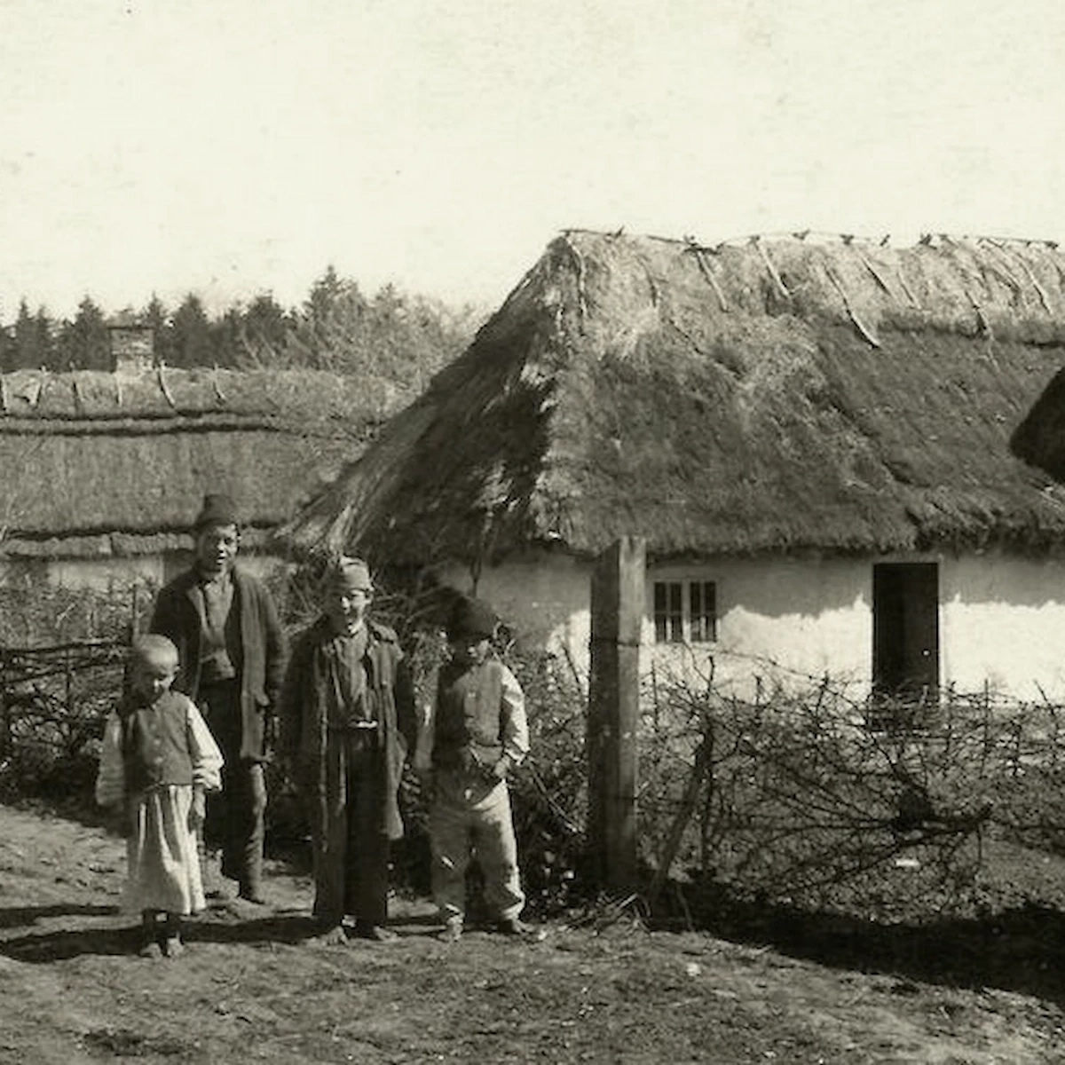Archiwalna fotografia mieszkańców przed tradycyjnym drewnianym domem krytym strzechą