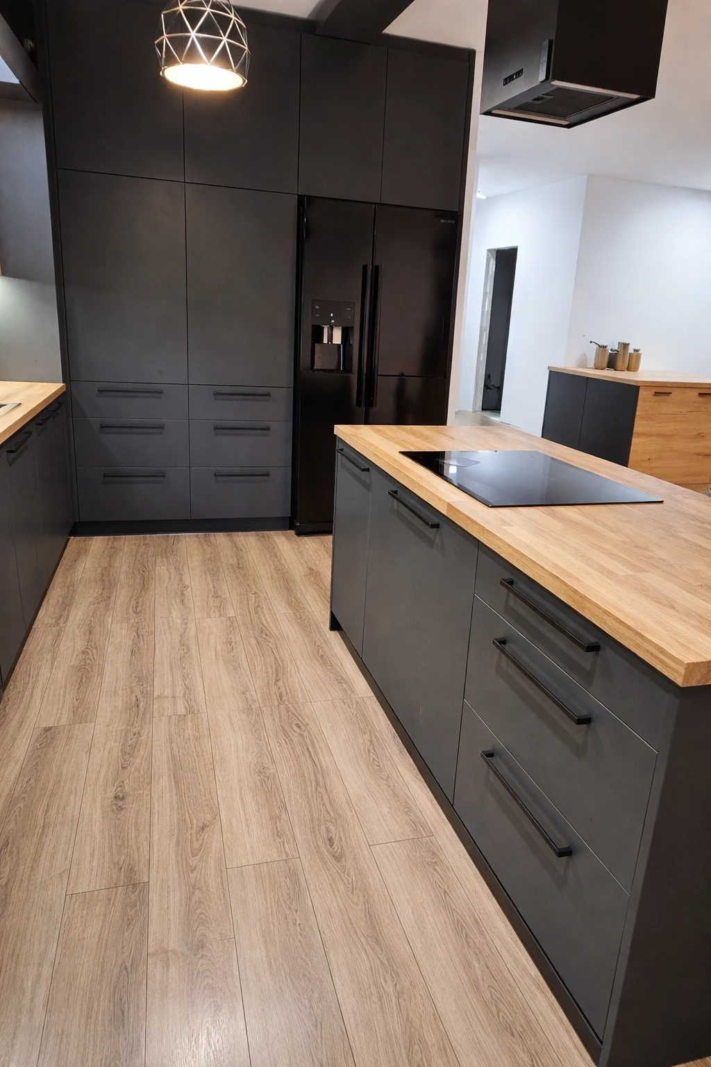 Loftowa kuchnia z ciemnymi frontami, wyspą i drewnianym blatem.