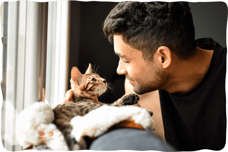 man smiling at cat near a window