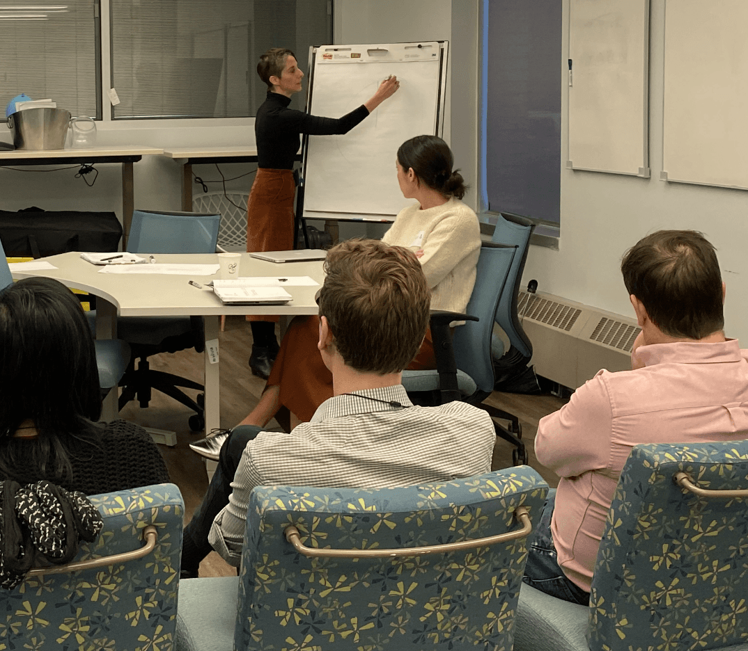 Public Works facilitator leads a human-centered, data-driven design thinking workshop using a flip chart as participants discuss organizational challenges and co-create strategies for product, service, and system transformation.