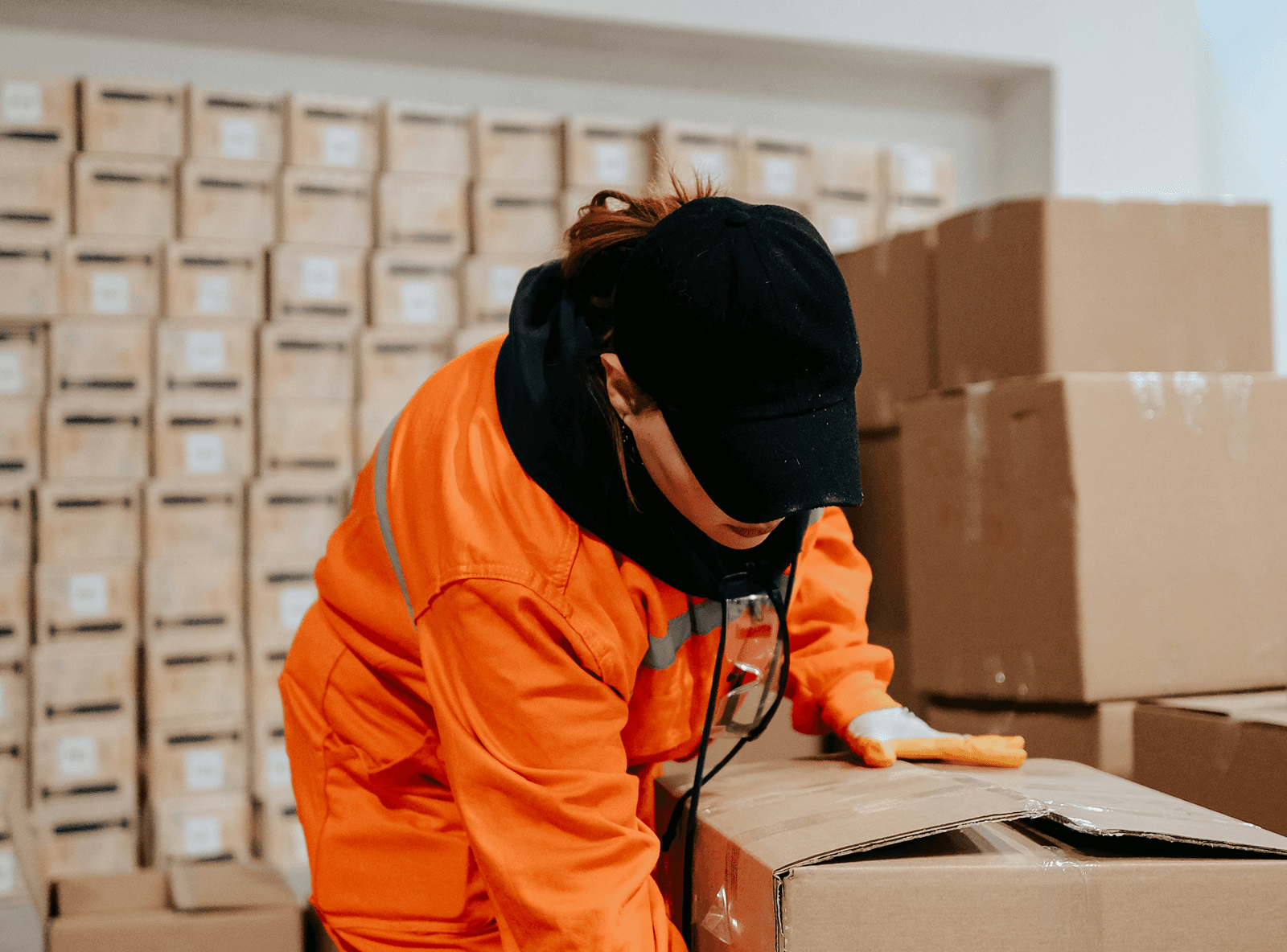 A warehouse worker in orange coveralls and a cap lifting a large box.