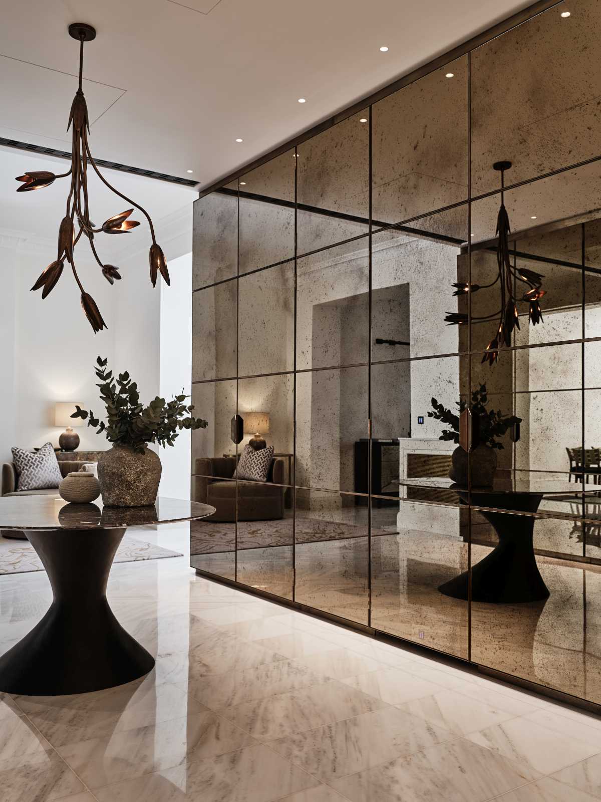 Heritage interior entrance hall updated by a London conservation architect, featuring an antiqued glass mirror wall and modern statement light fixture.