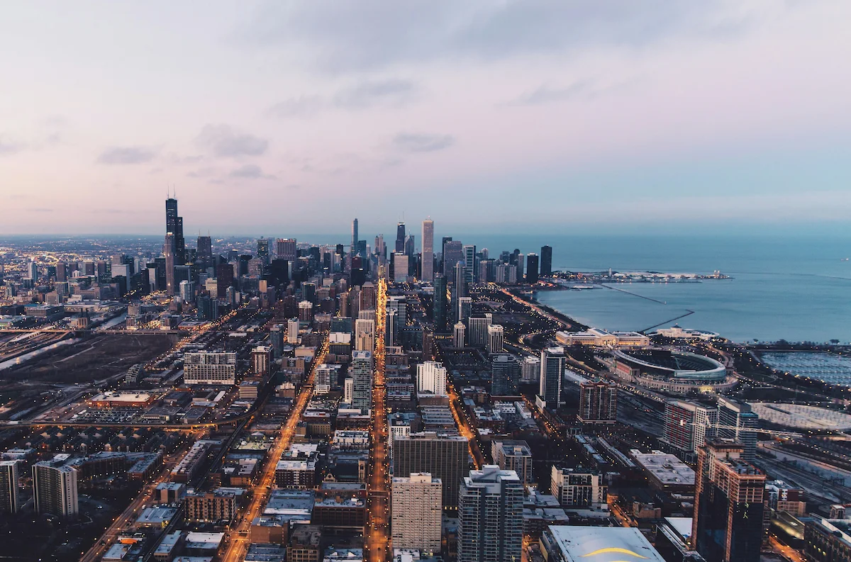 Aerial view of the Chicago skyline along Lake Michigan, showing dense downtown towers at sunset.