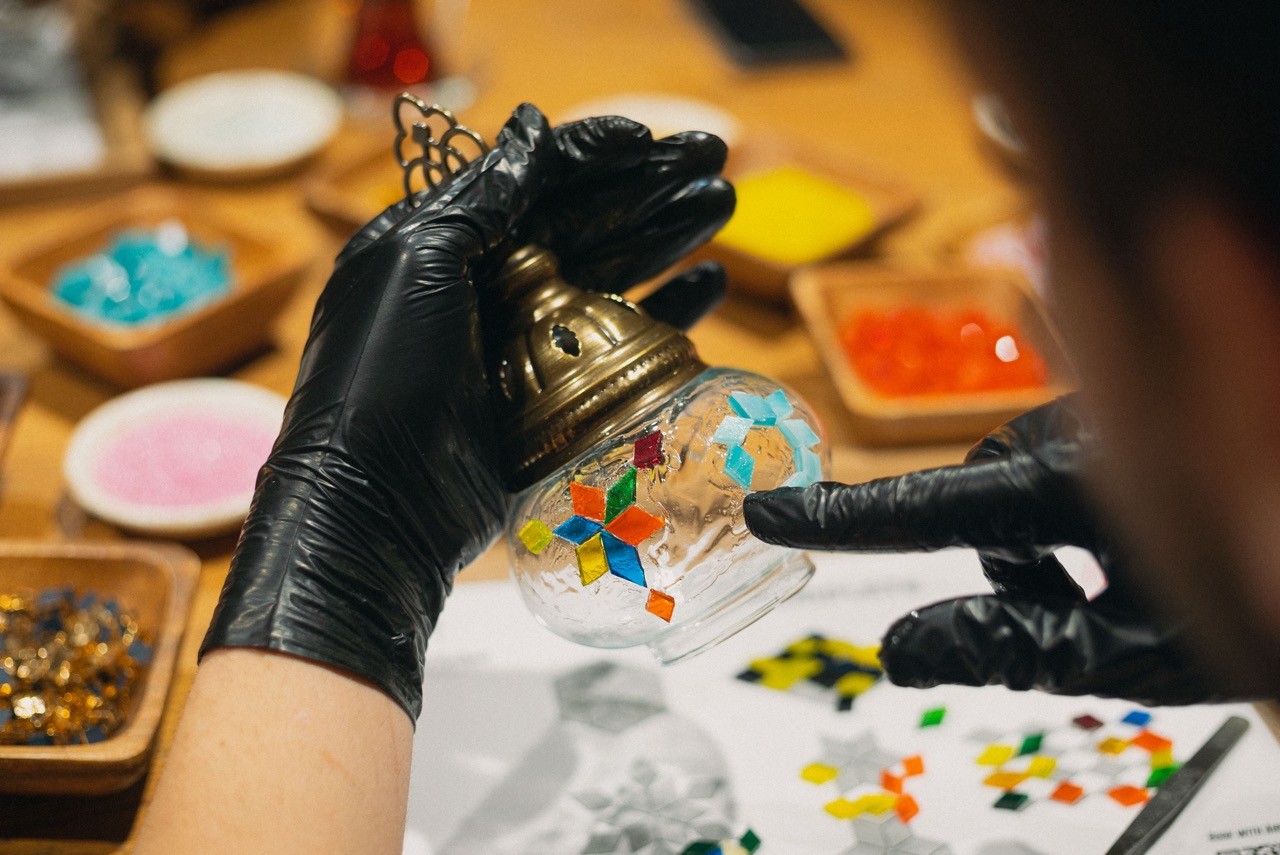 Person wearing black gloves decorates a glass Turkish lamp with colorful mosaic tiles in a Turkish Lamp Making Class in Istanbul.