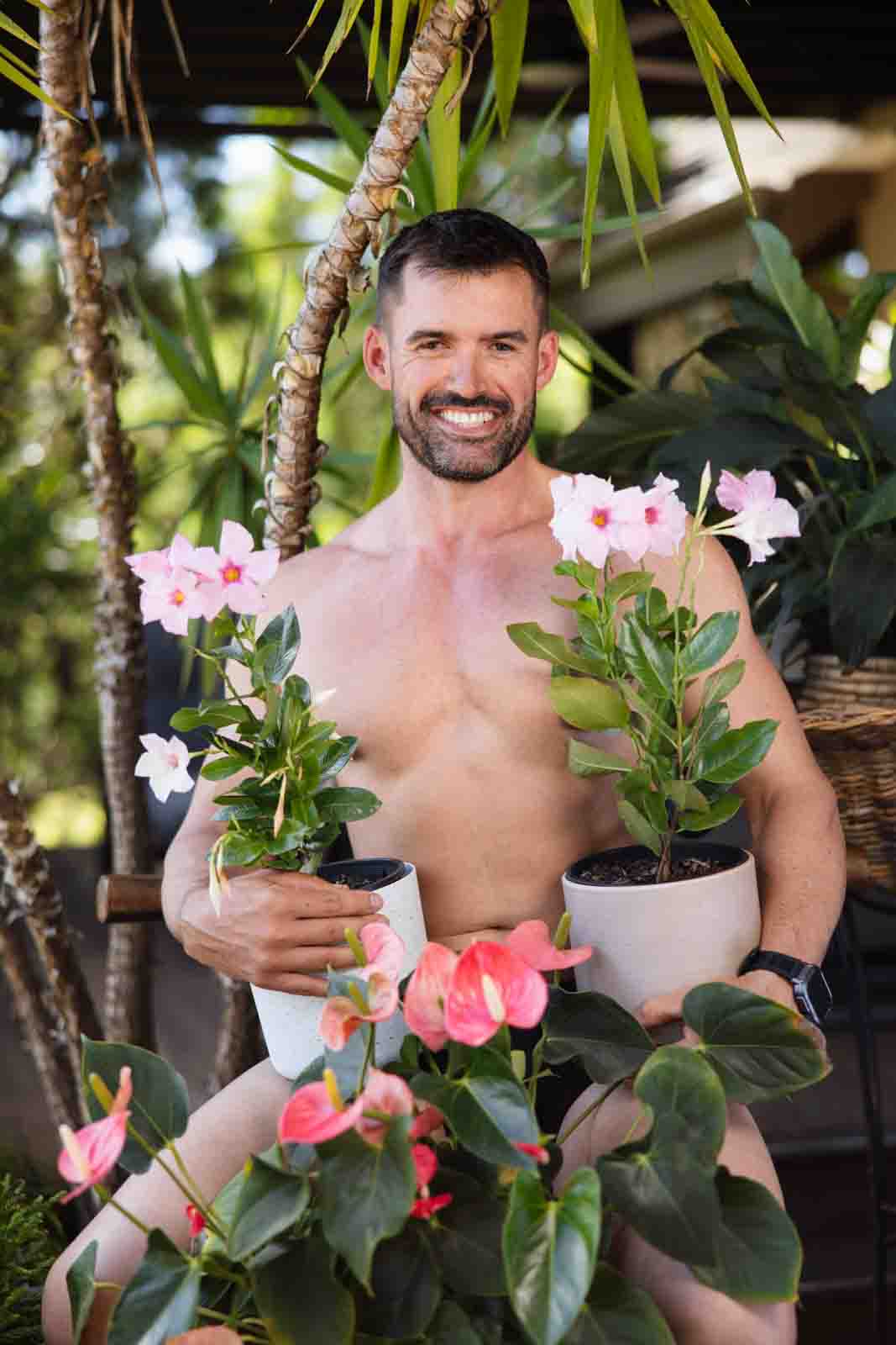 Shirtless man sitting on stool surrounded by plants