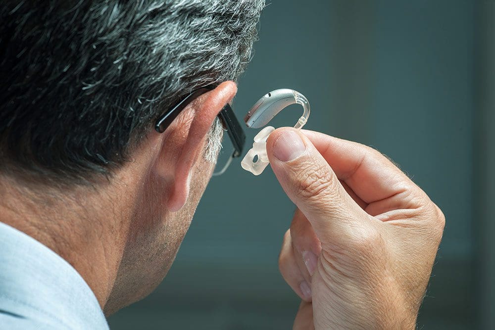 Person using a magnifying glass to examine their ear closely, with a neutral background.