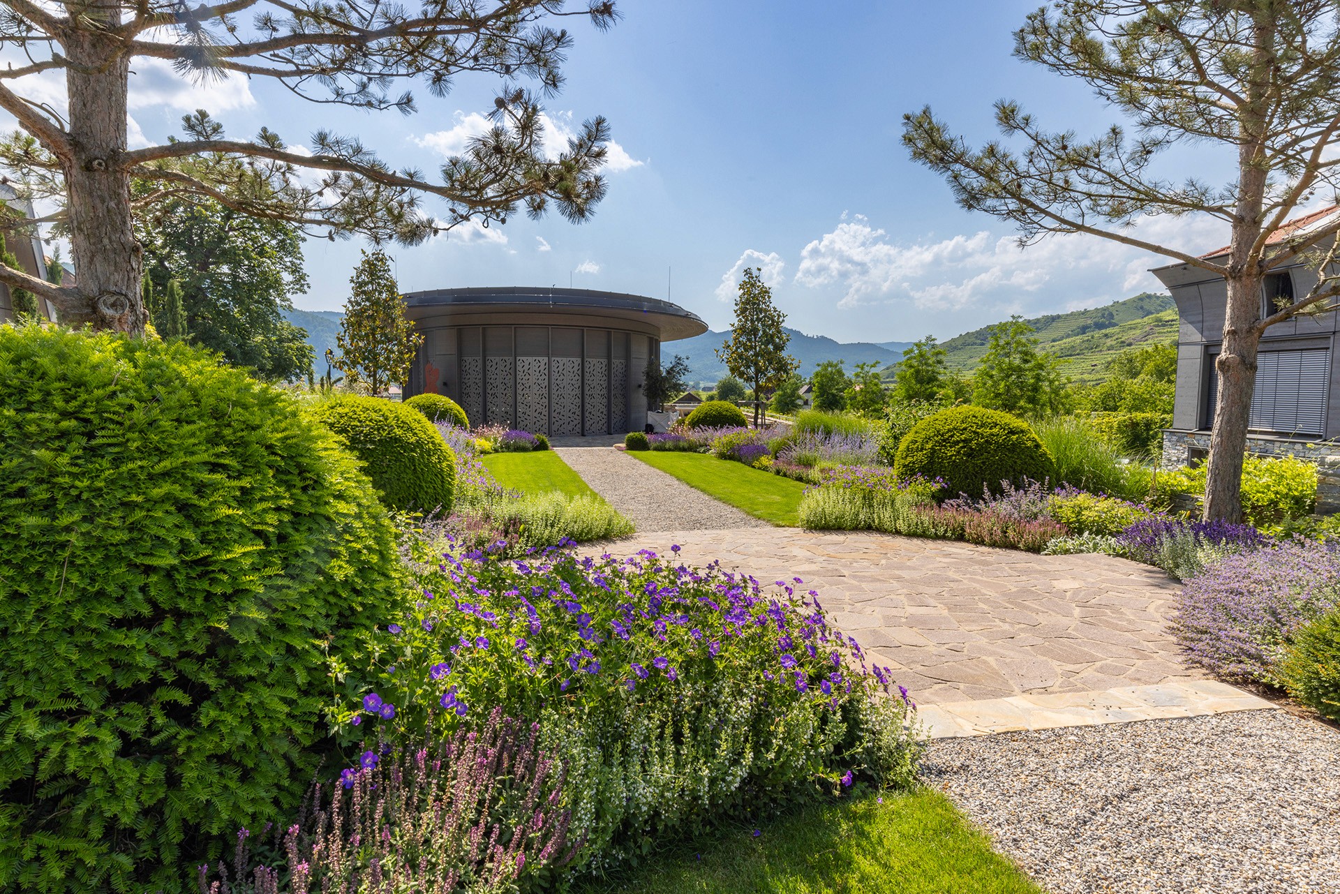 Symmetrisch angelegter Garten mit Rasenflächen, Kieswegen und Blick auf die umliegende Landschaft.