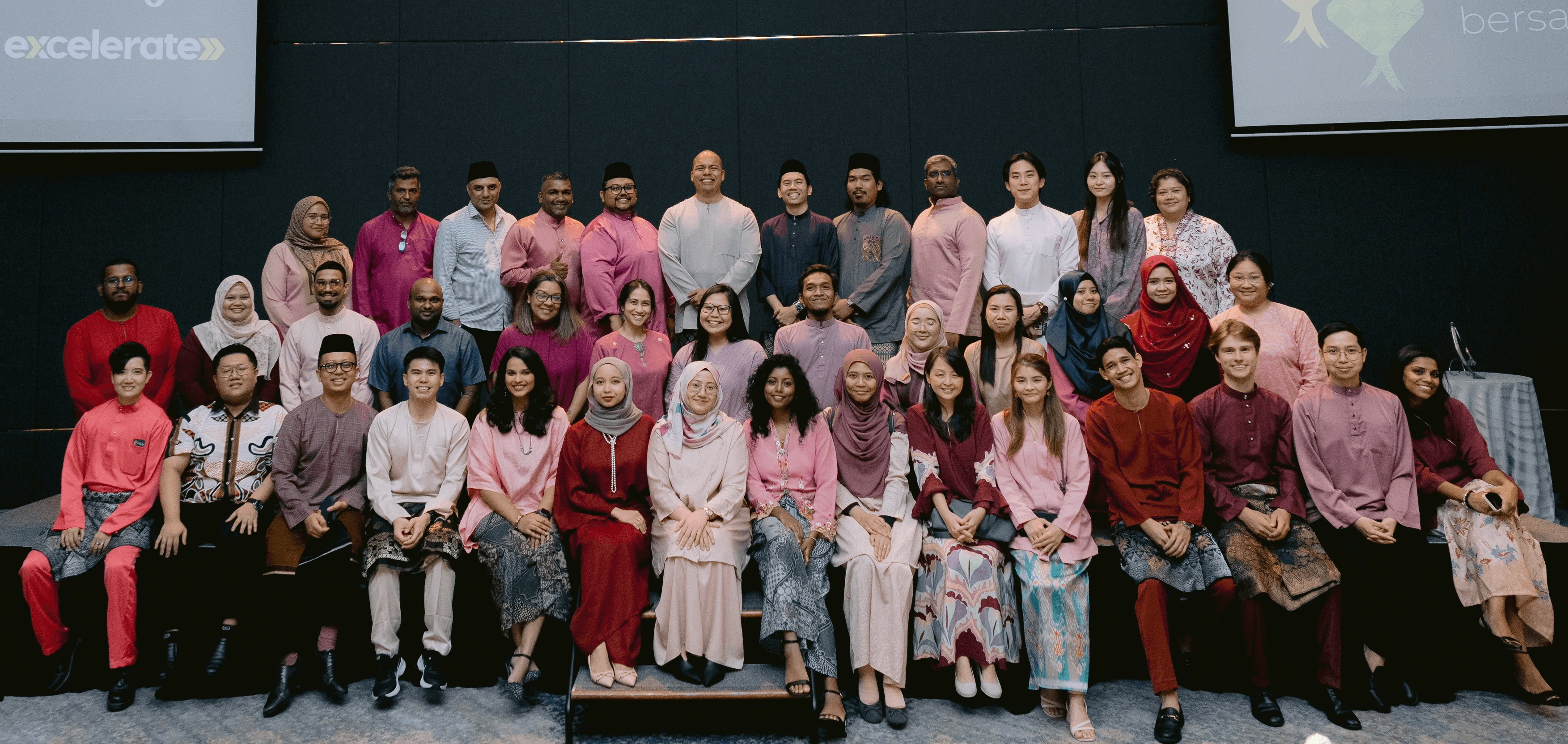 A diverse group of individuals in traditional attire poses together on a staircase, smiling in a modern interior setting.