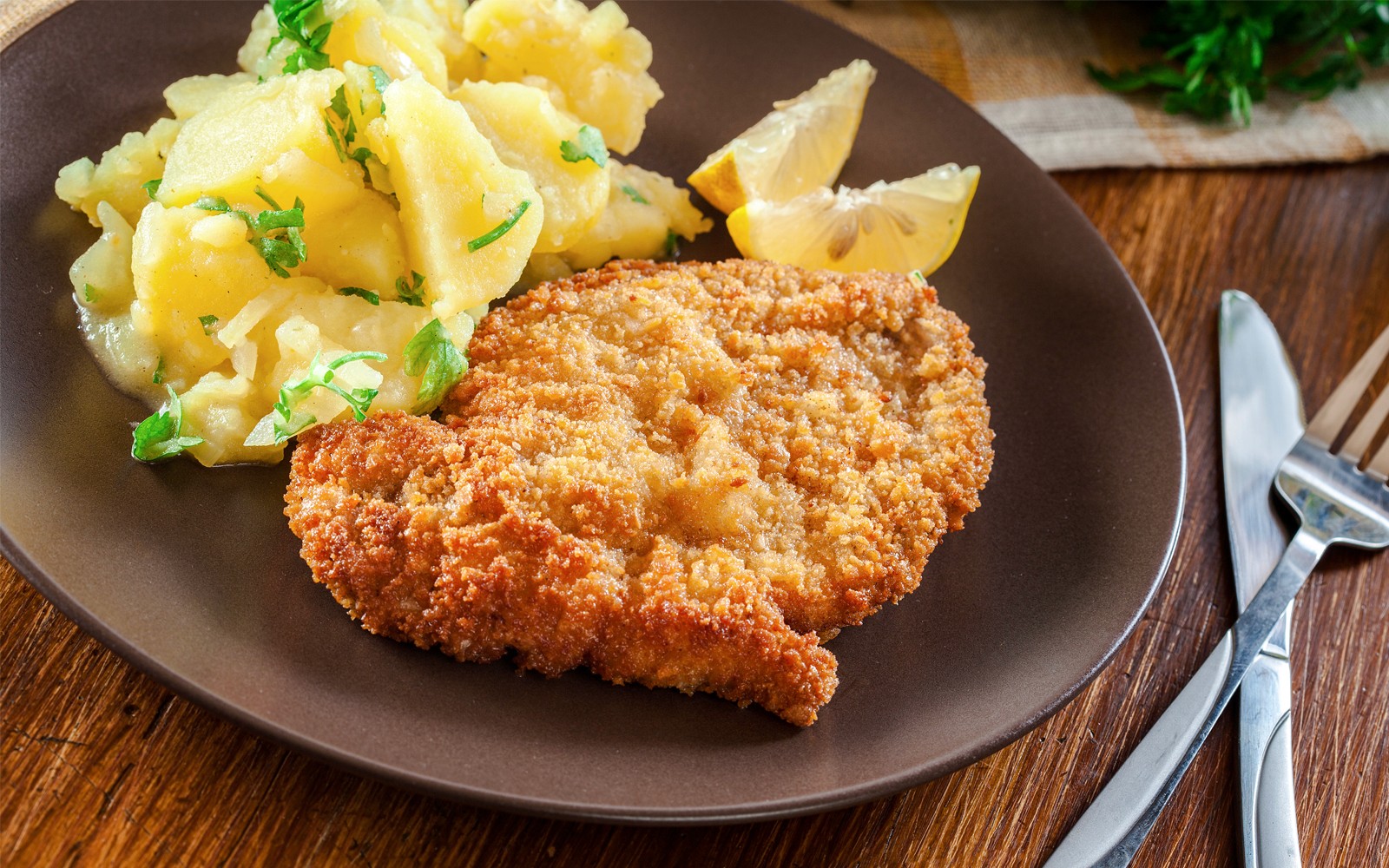 Wienerschnitzel med kartoffelsalat og citronskiver på en tallerken.