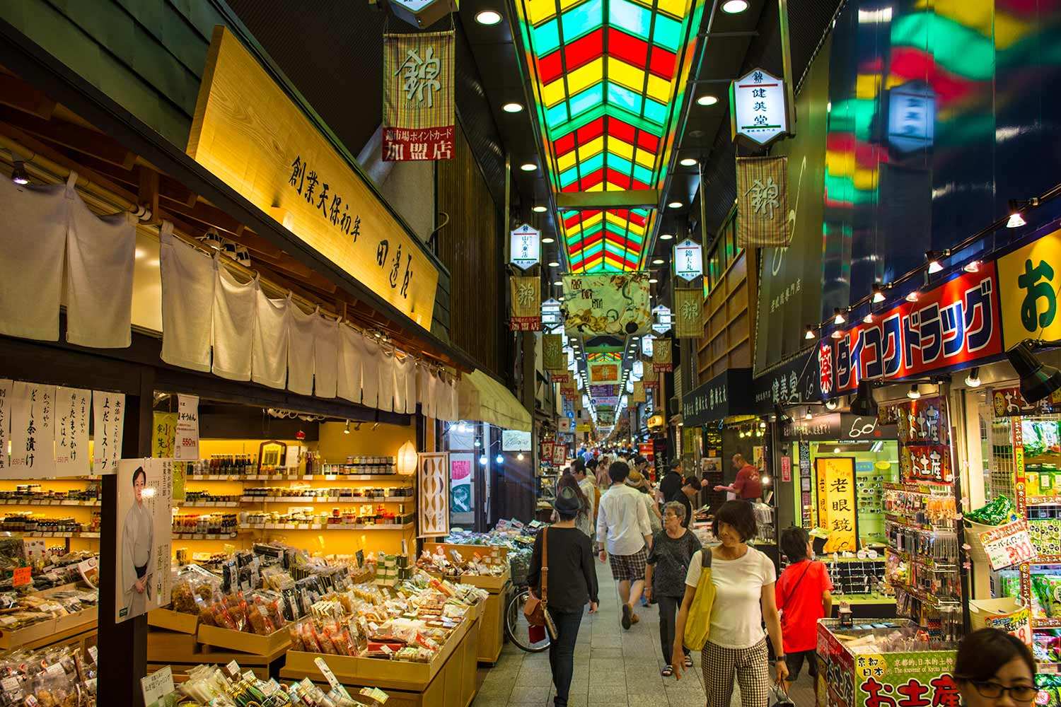Crowded Japanese shopping street at night with colorful overhead lanterns and illuminated storefronts selling goods.