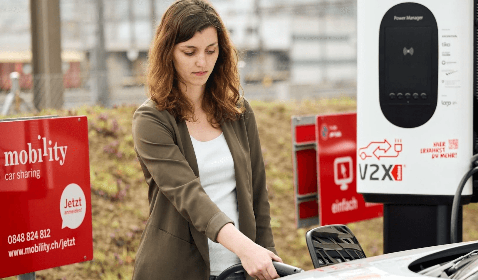 Young woman charging an electric vehicle at a Mobility car-sharing station, highlighting the integration of electric mobility and car-sharing services in Switzerland