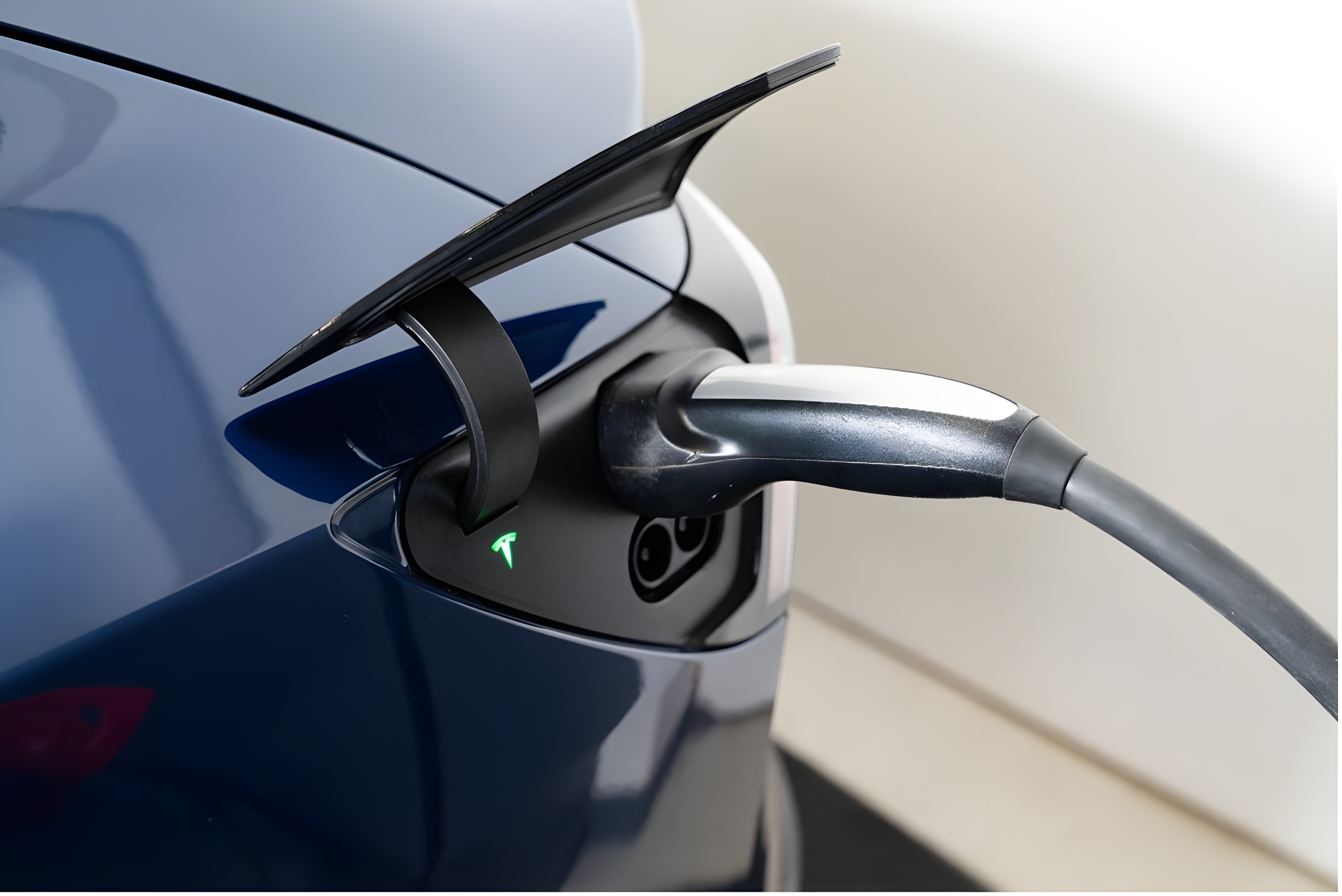 Tesla en cours de recharge, détail du port de charge avec connecteur branché sur carrosserie bleue