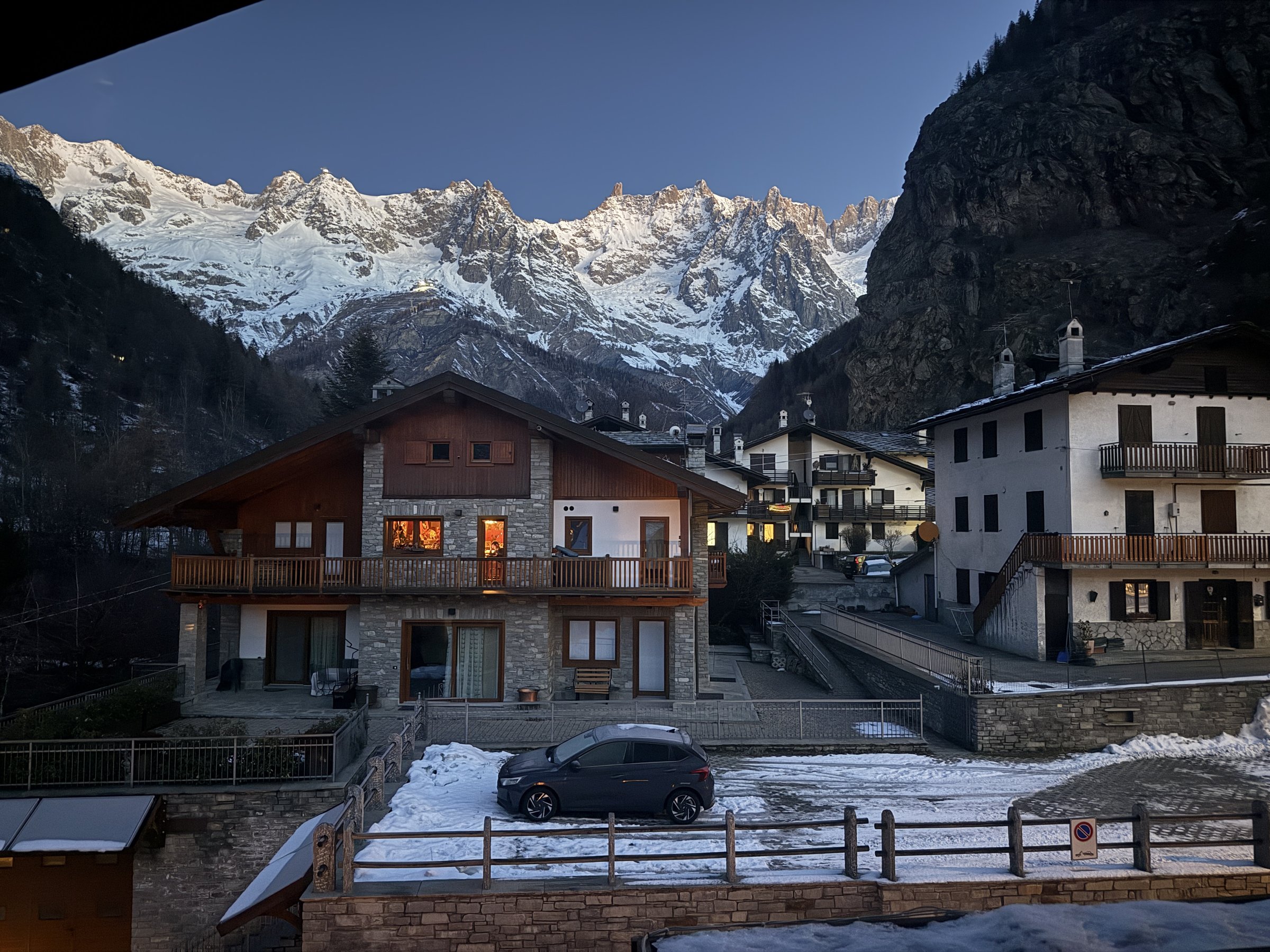 Dawn light on the snow-covered Mont Blanc massif above stone chalets in a village near Courmayeur, Italy