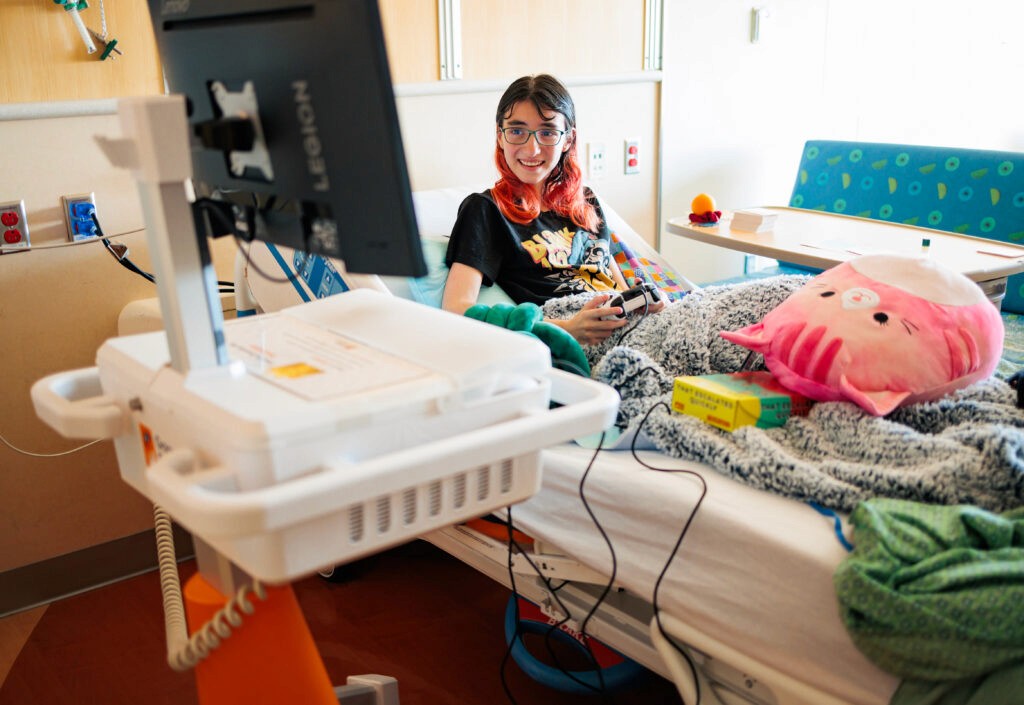 A patient sits in their hospital bed while enjoying games on a GO Kart.